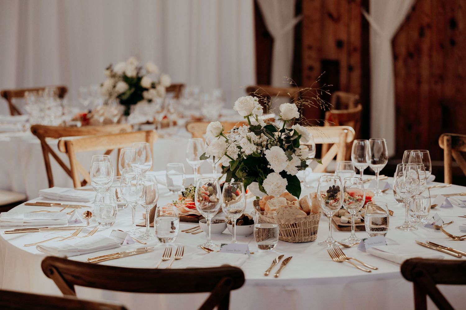 Sophisticated wedding reception table with white rose centerpiece, crystal glasses, and gold flatware settings.