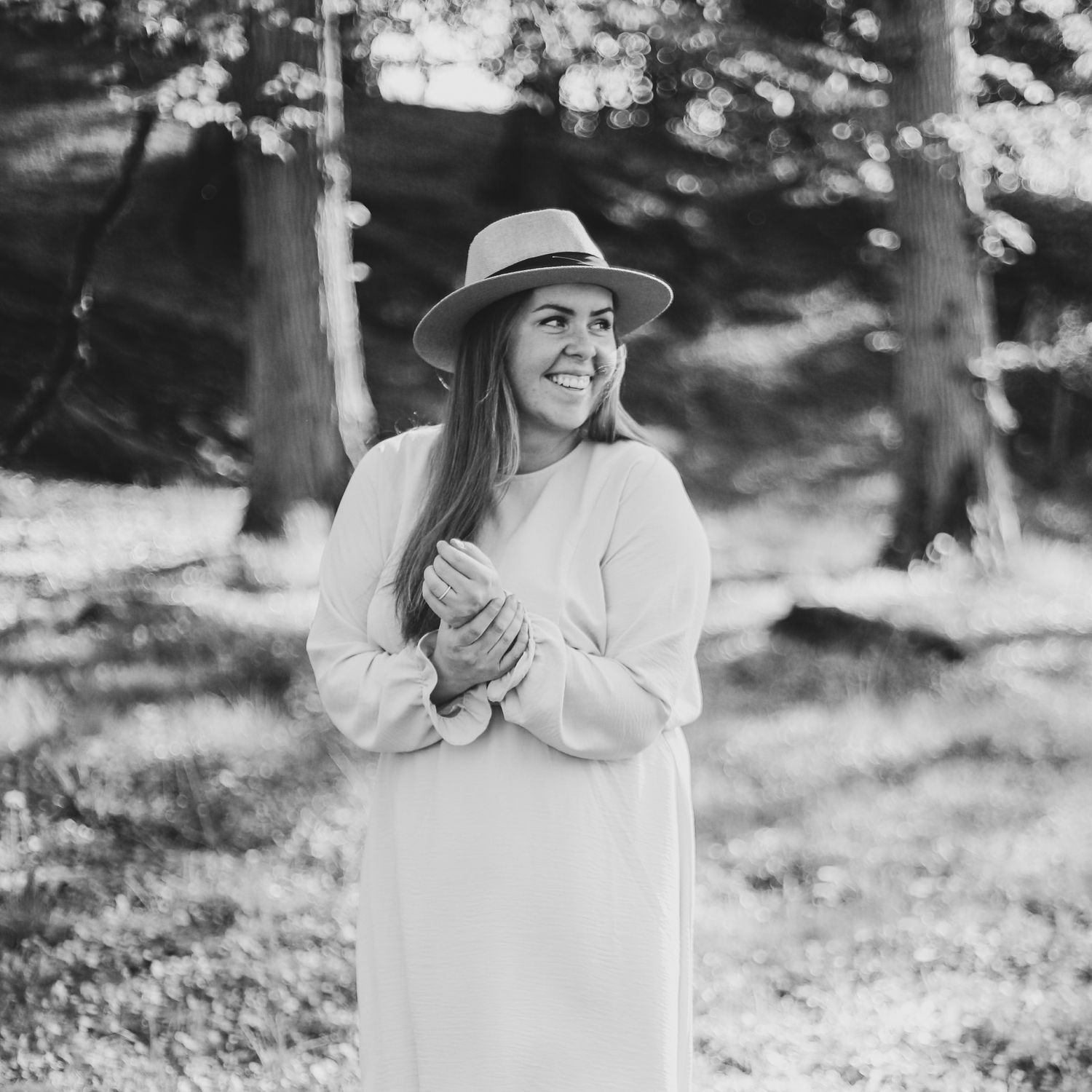 Black and white portrait of a smiling woman in a white dress and hat outdoors.