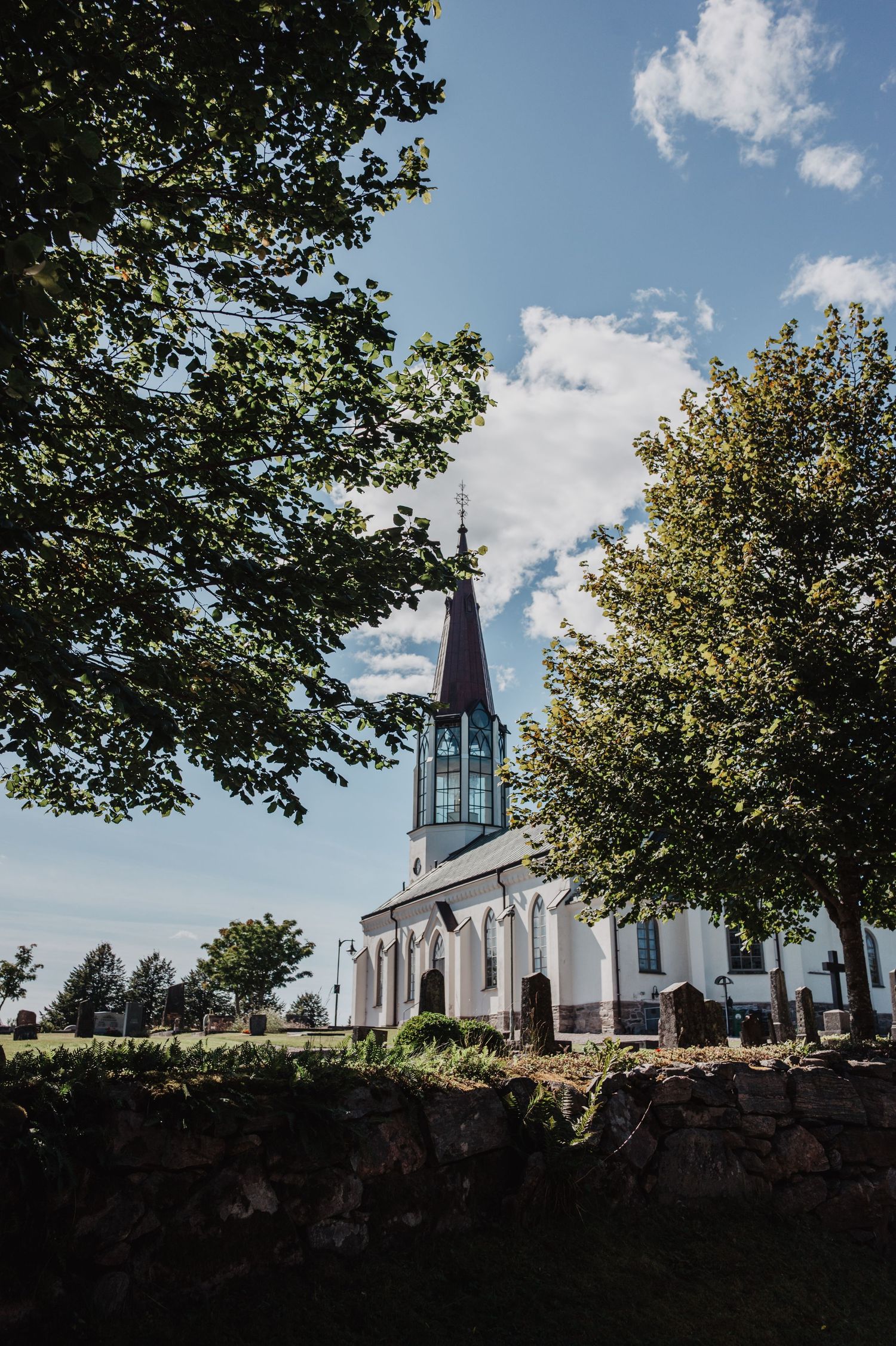 White Swedish church with pointed steeple surrounded by trees under a blue sky.