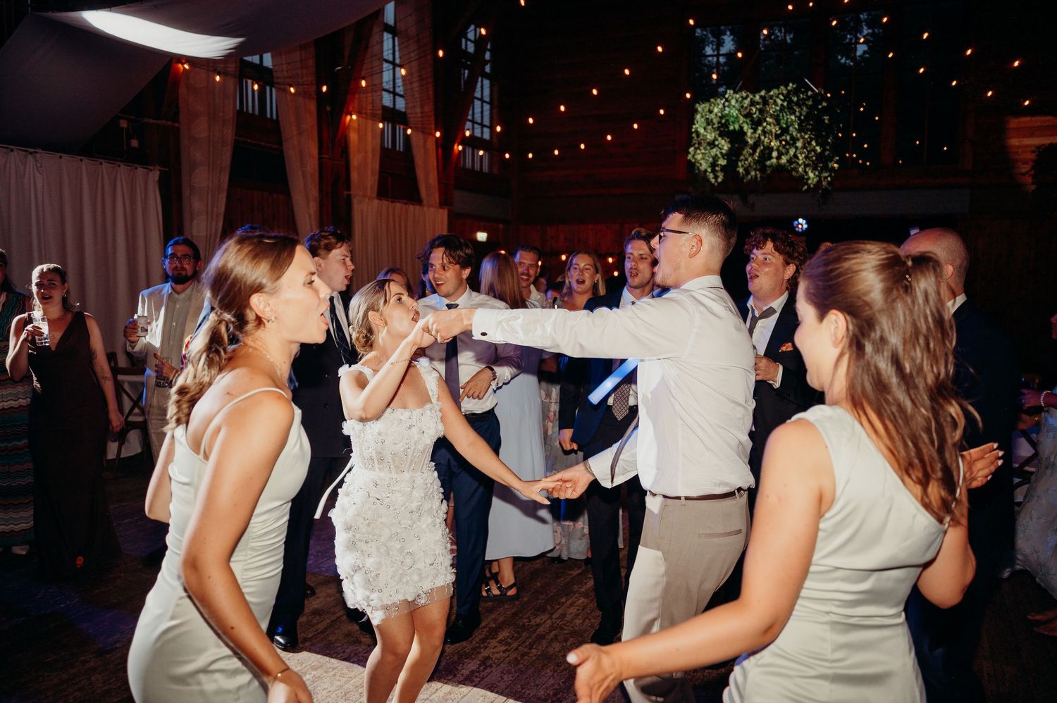 Guests dance joyfully together under string lights on the wedding reception dance floor.