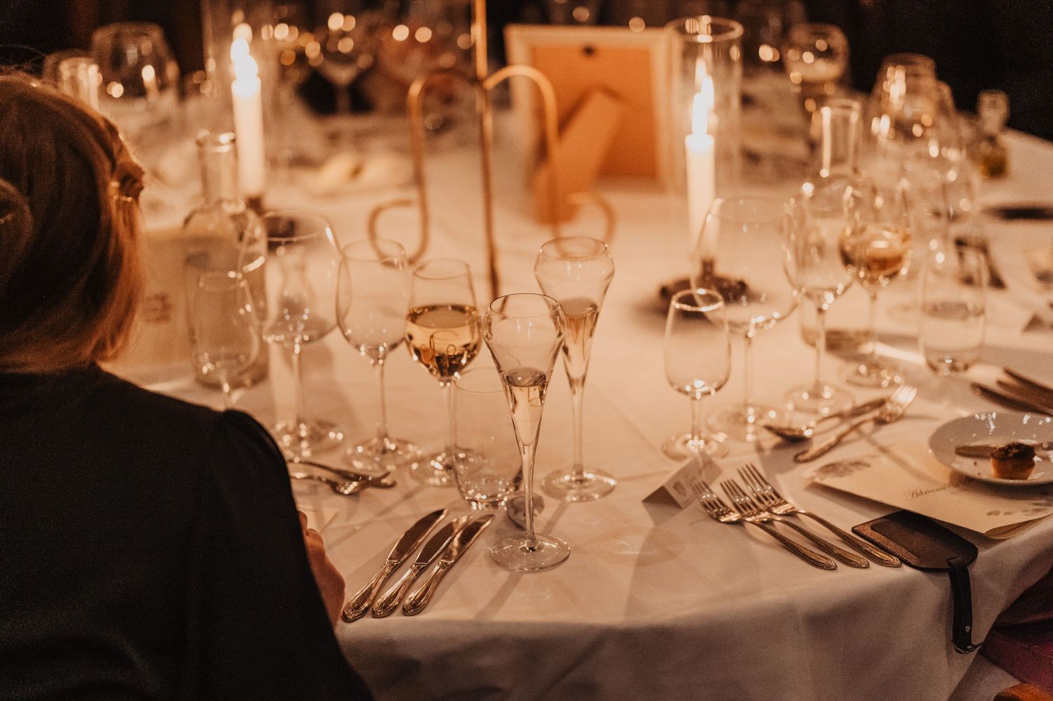 Elegant wedding reception table set with crystal glassware, silver cutlery, and tall candles.