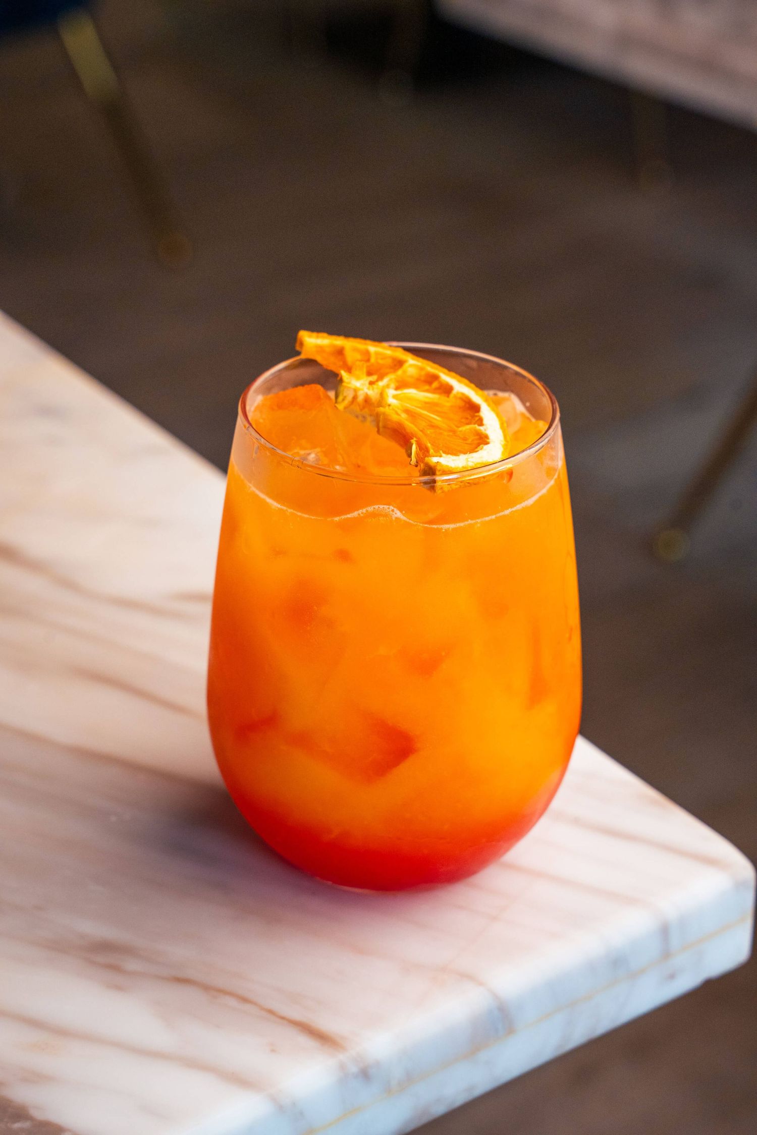Bright orange aperol spritz cocktail served on marble coaster with citrus garnish.