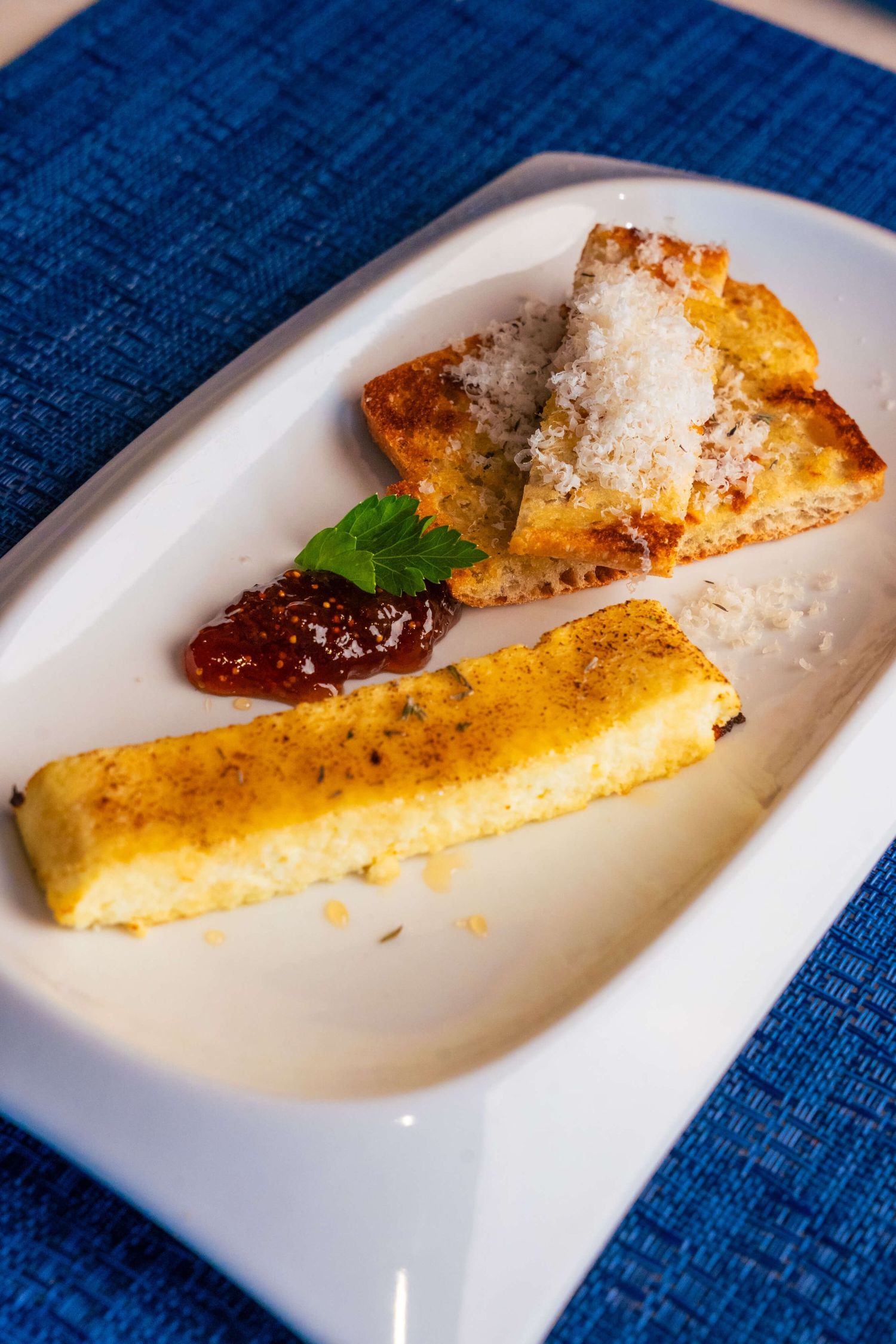 Plated polenta sticks with marinara sauce and parmesan cheese on a white dish with blue tablecloth.