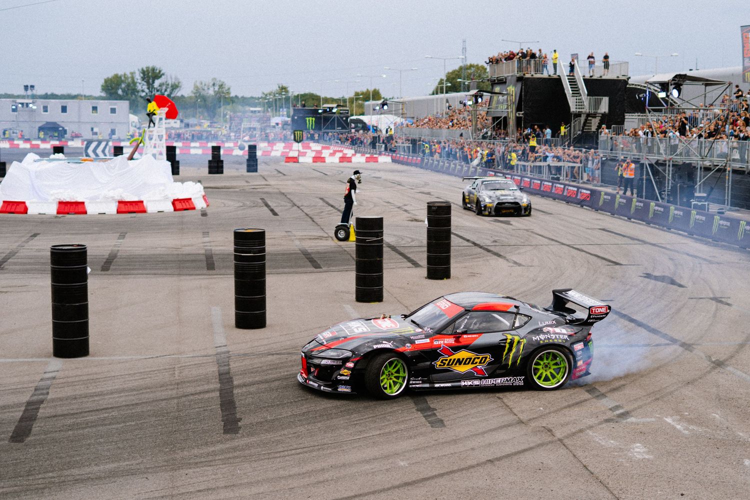 Racing cars perform synchronized drifting maneuvers on a concrete track.