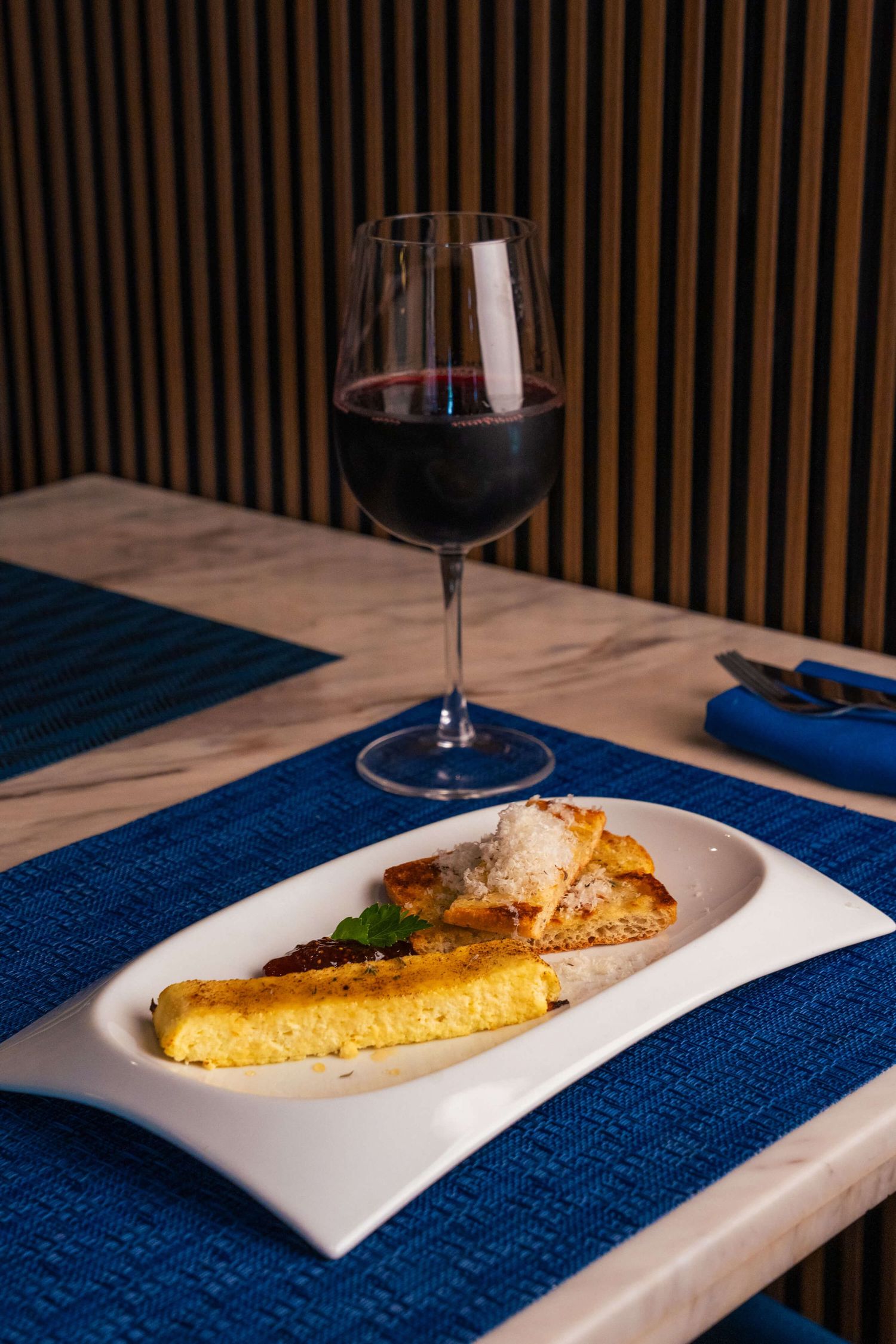 Golden brown quiche or tart served on a white plate with red wine glass in background.