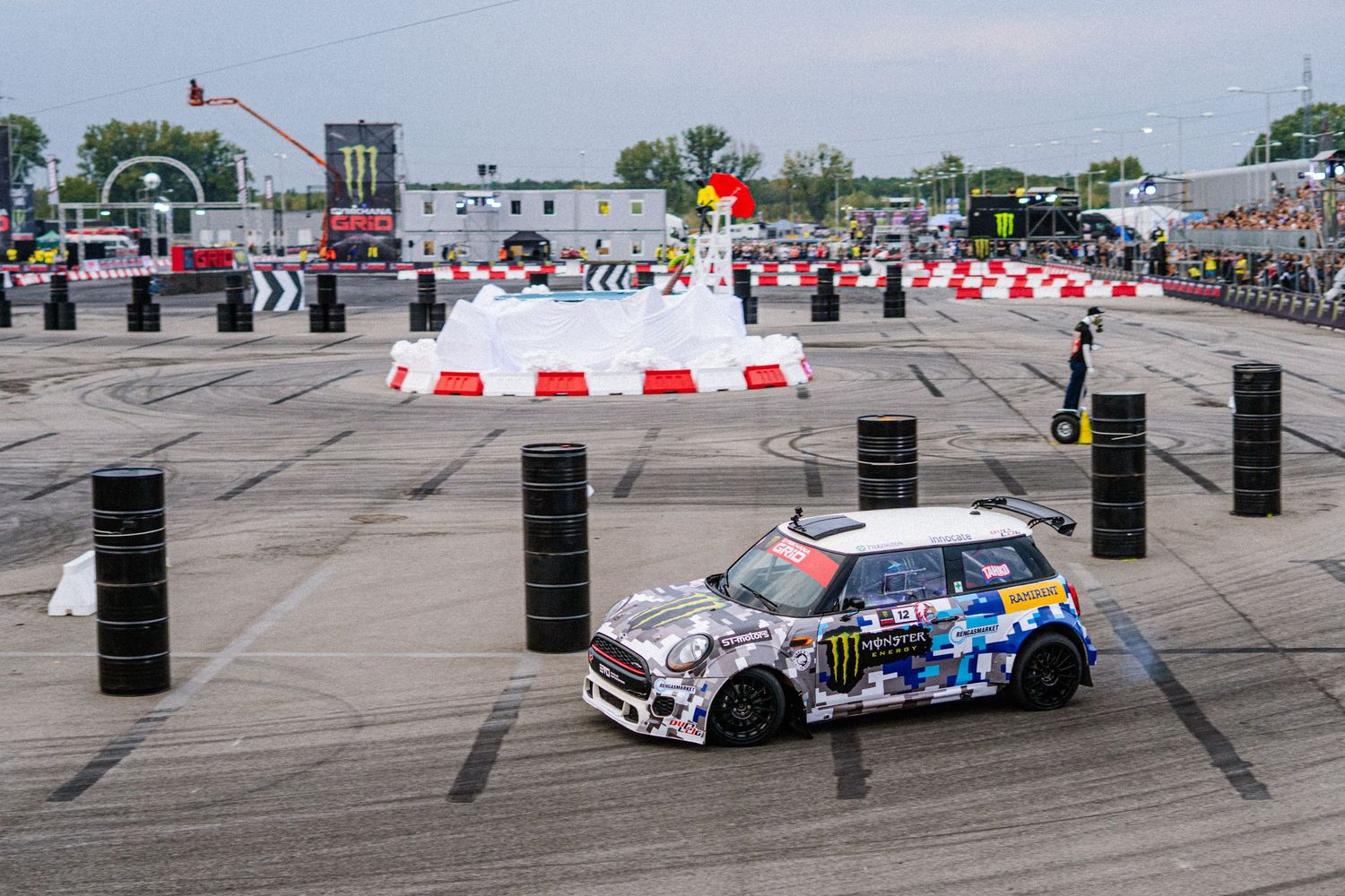 Professional drift cars compete on a course marked with safety barriers and pylons.