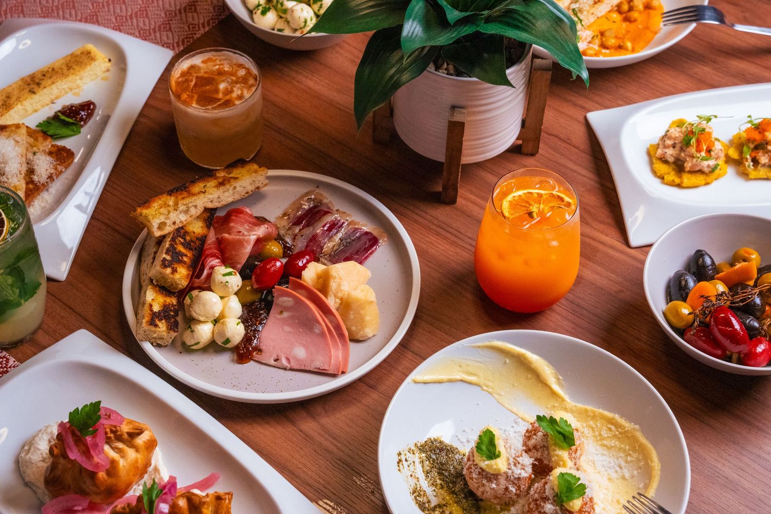 A wooden table filled with various brunch dishes, cocktails, and appetizers in a restaurant setting.