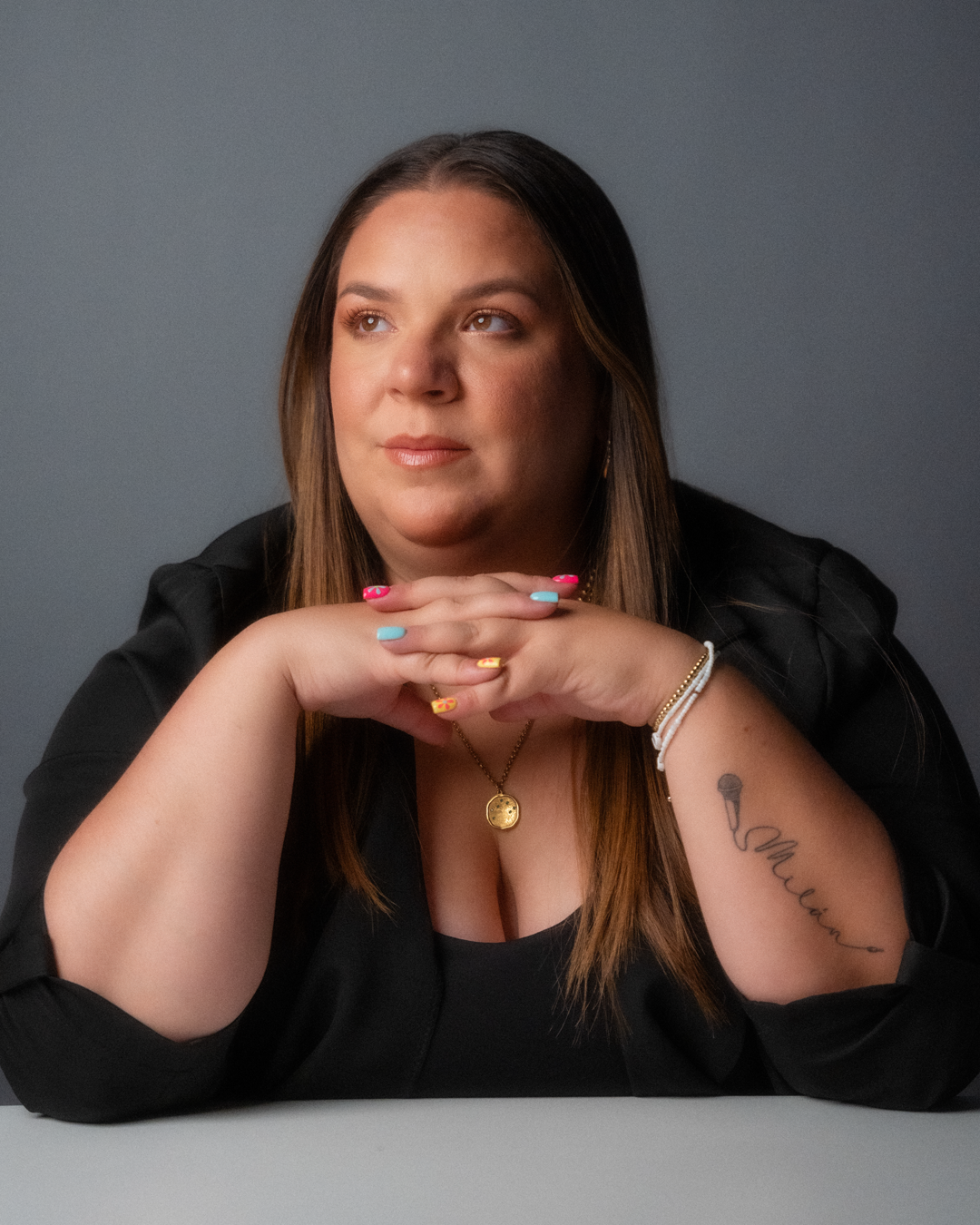 Studio portrait with black blazer and minimalist jewelry against grey background.