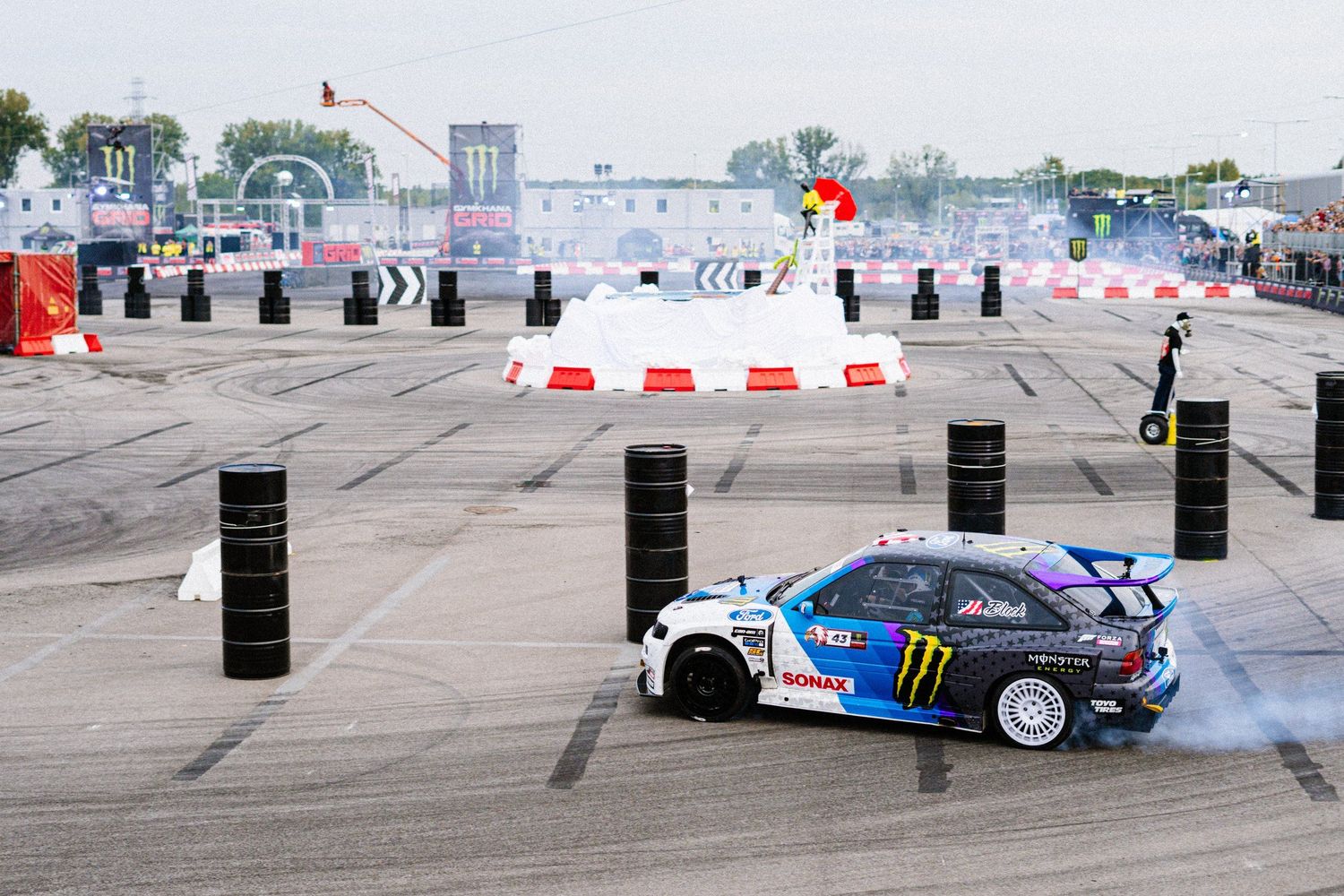 Racing car performing drift maneuvers on a track with safety barriers.