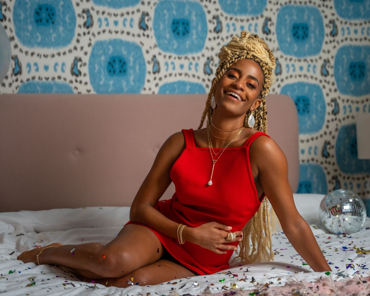 Fashion portrait on a bed with blue patterned wallpaper and scattered rose petals.