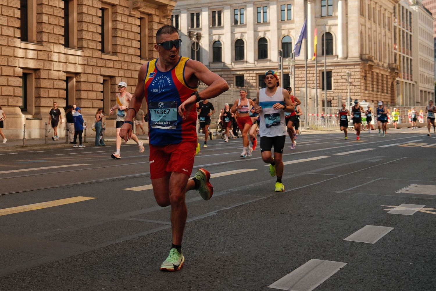 Urban marathon runners competing on a street lined with historic stone buildings.