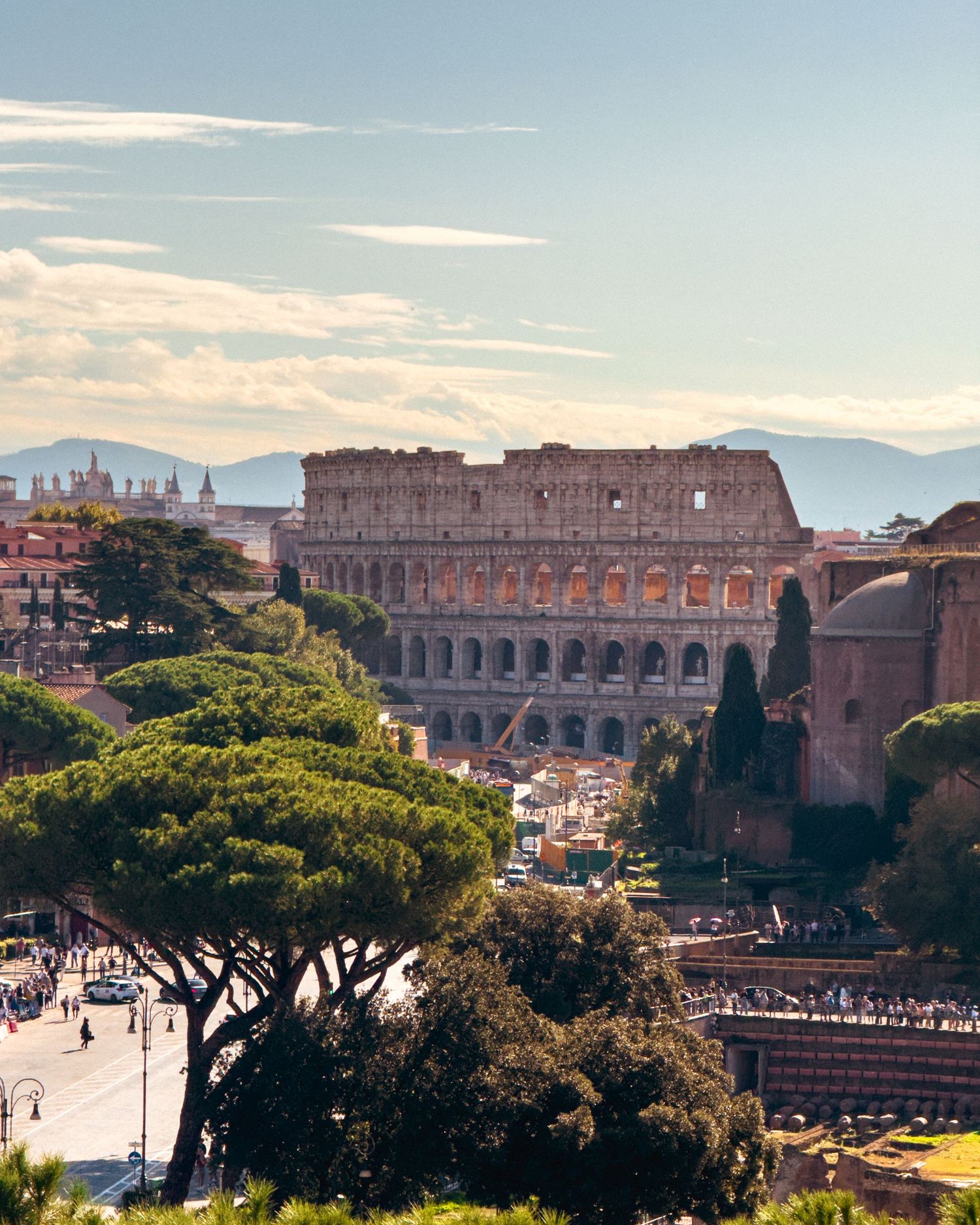 Panoramic view of the Roman Colosseum and surrounding architecture under blue sky.