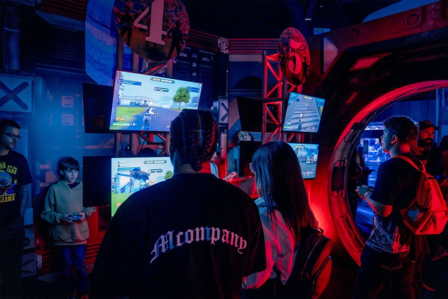Gaming event venue with audience watching large screens in dark room with red accent lighting.