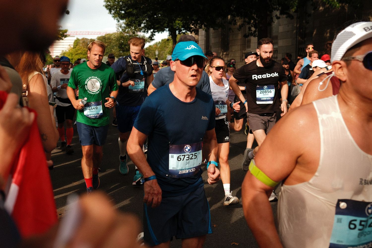 Marathon participants running through a sunny city street with spectators cheering from the sidelines.