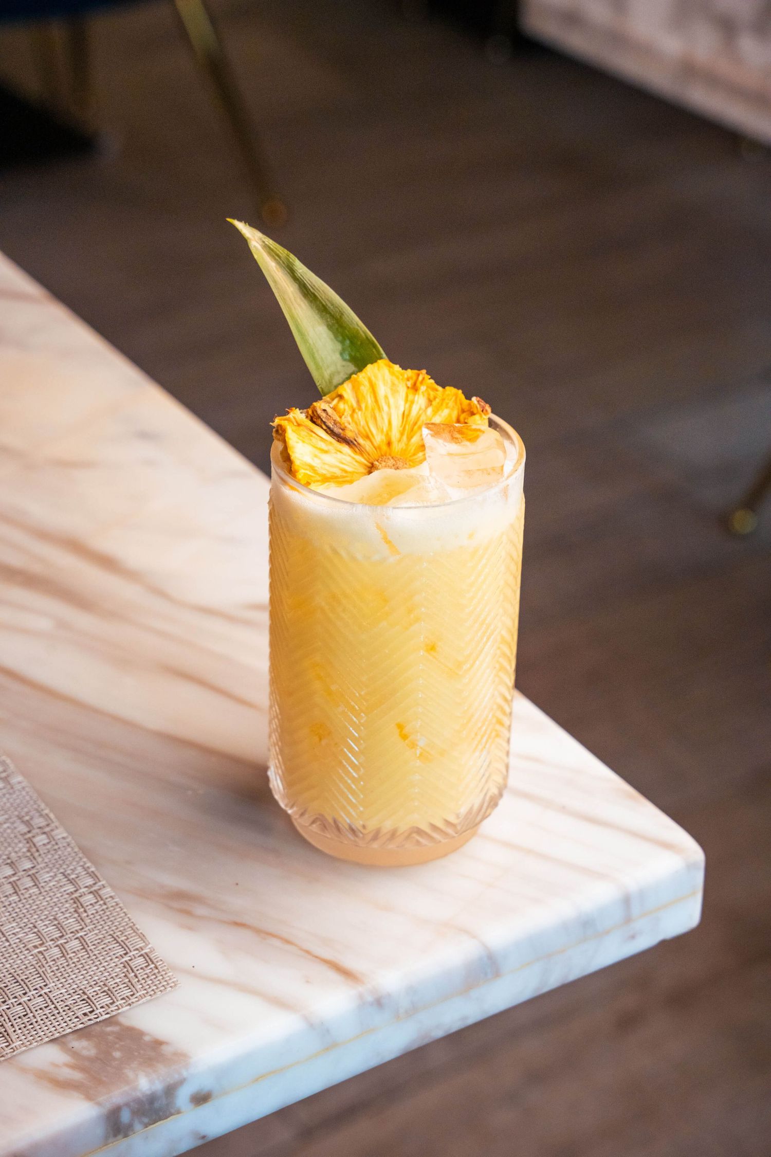 Yellow tropical cocktail garnished with fresh pineapple and citrus in an etched glass.