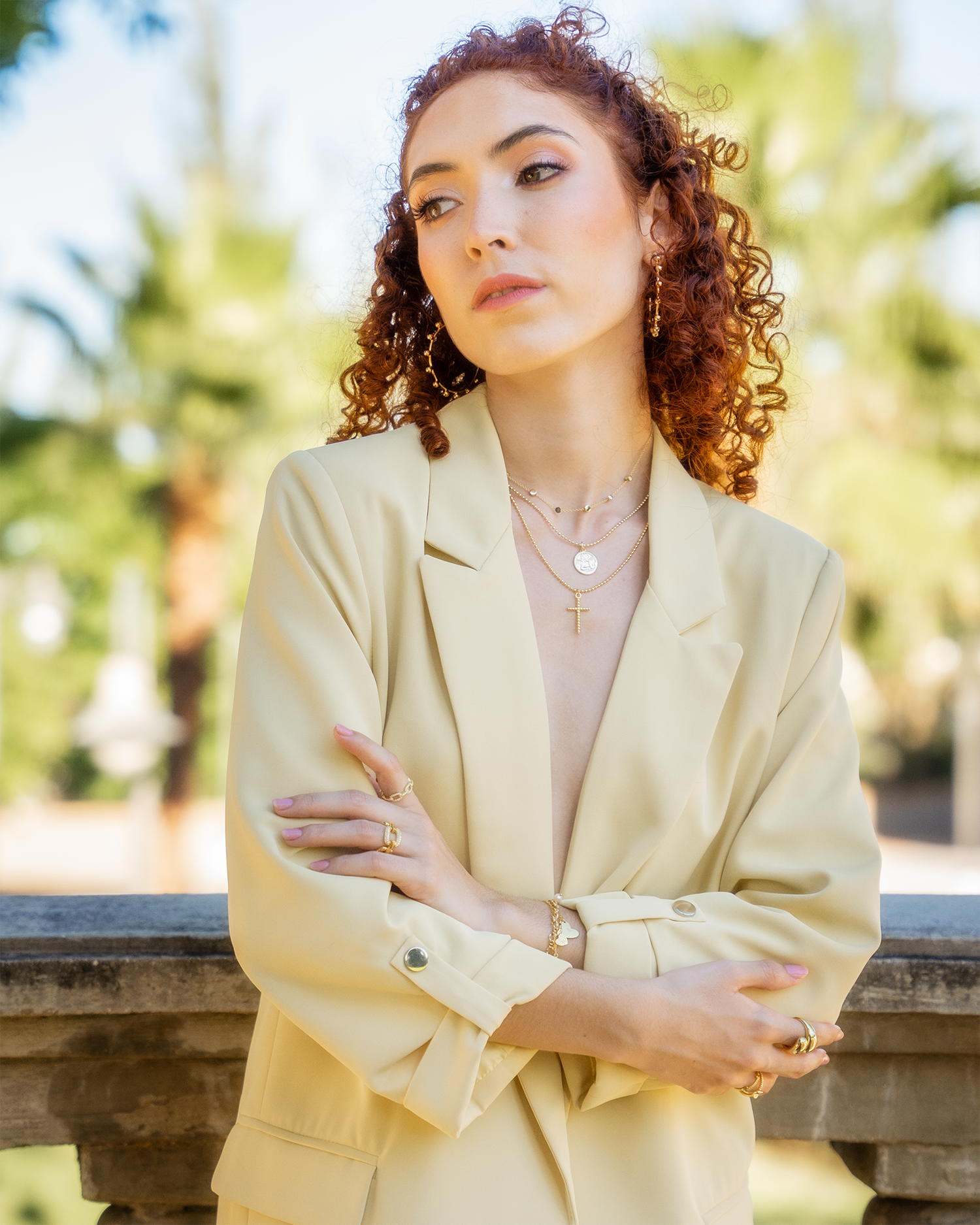 Professional portrait in cream blazer with layered necklaces against tropical background.