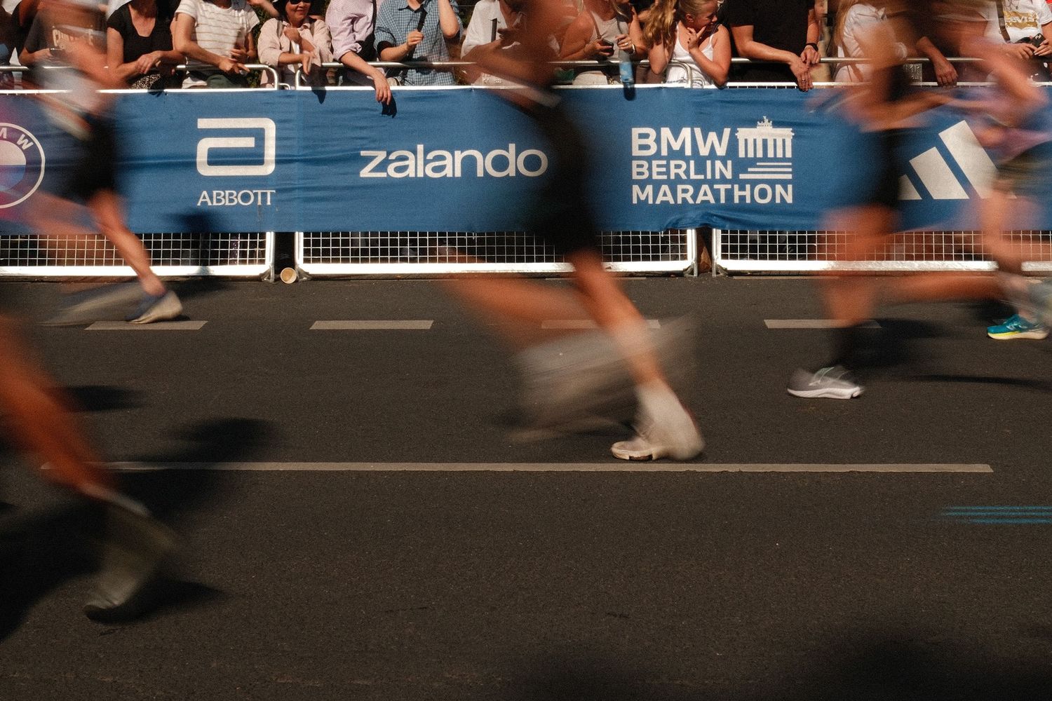 Berlin Marathon runners' feet blur across pavement during an urban race with Zalando and BMW event banners visible.