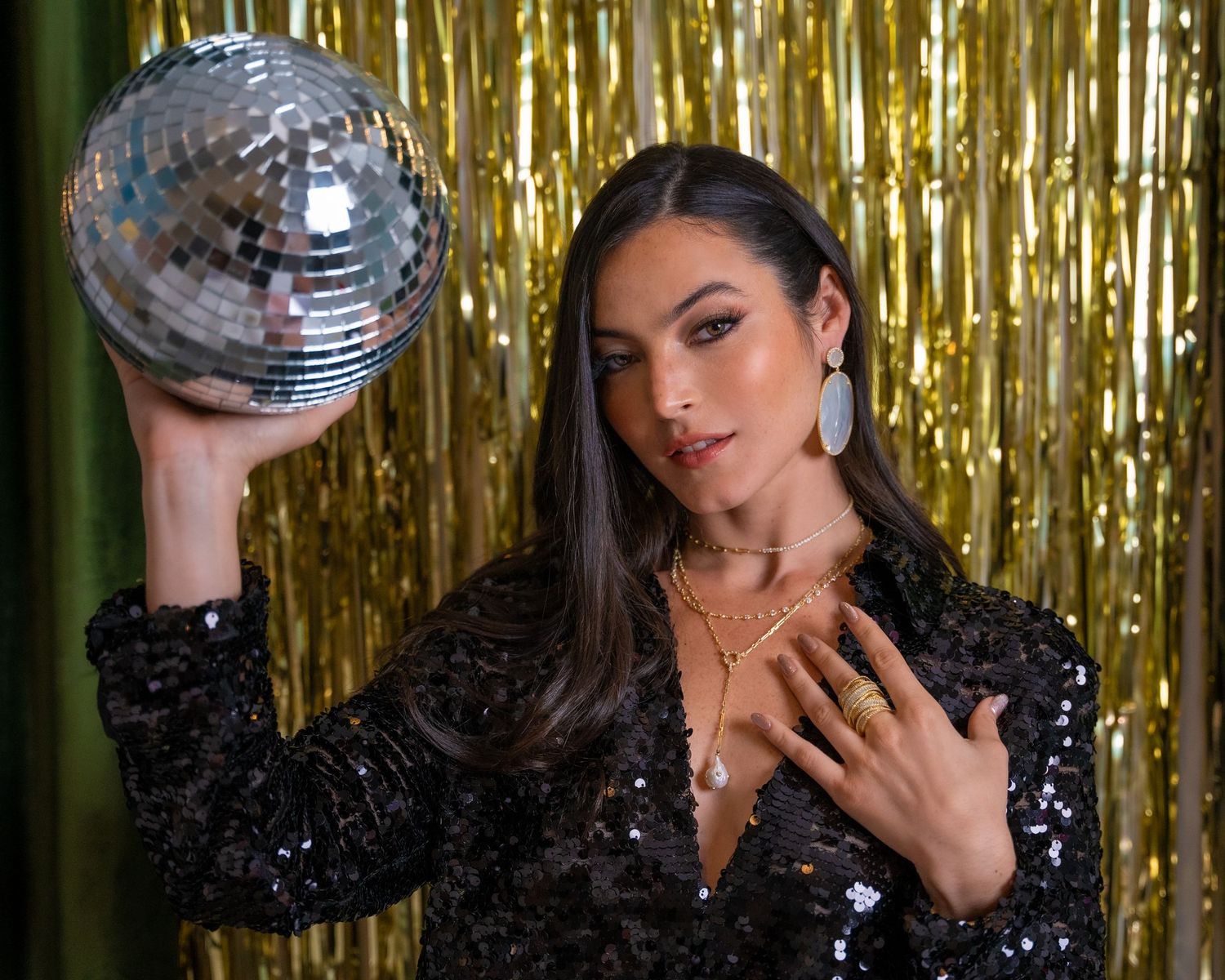 Glamorous portrait with a disco ball against a gold tinsel backdrop.