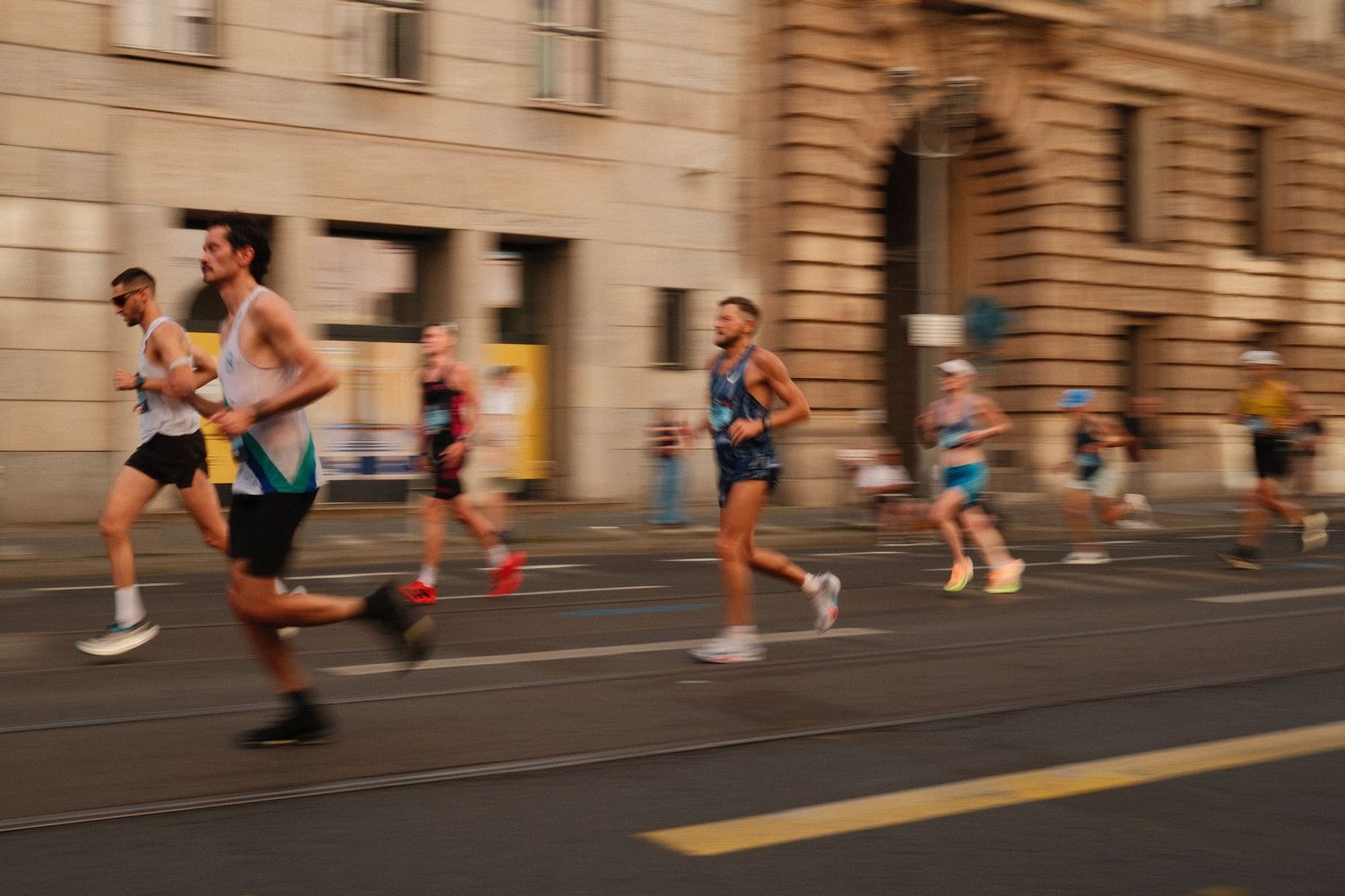 Marathon competitors running on asphalt street past beige stone building facade.