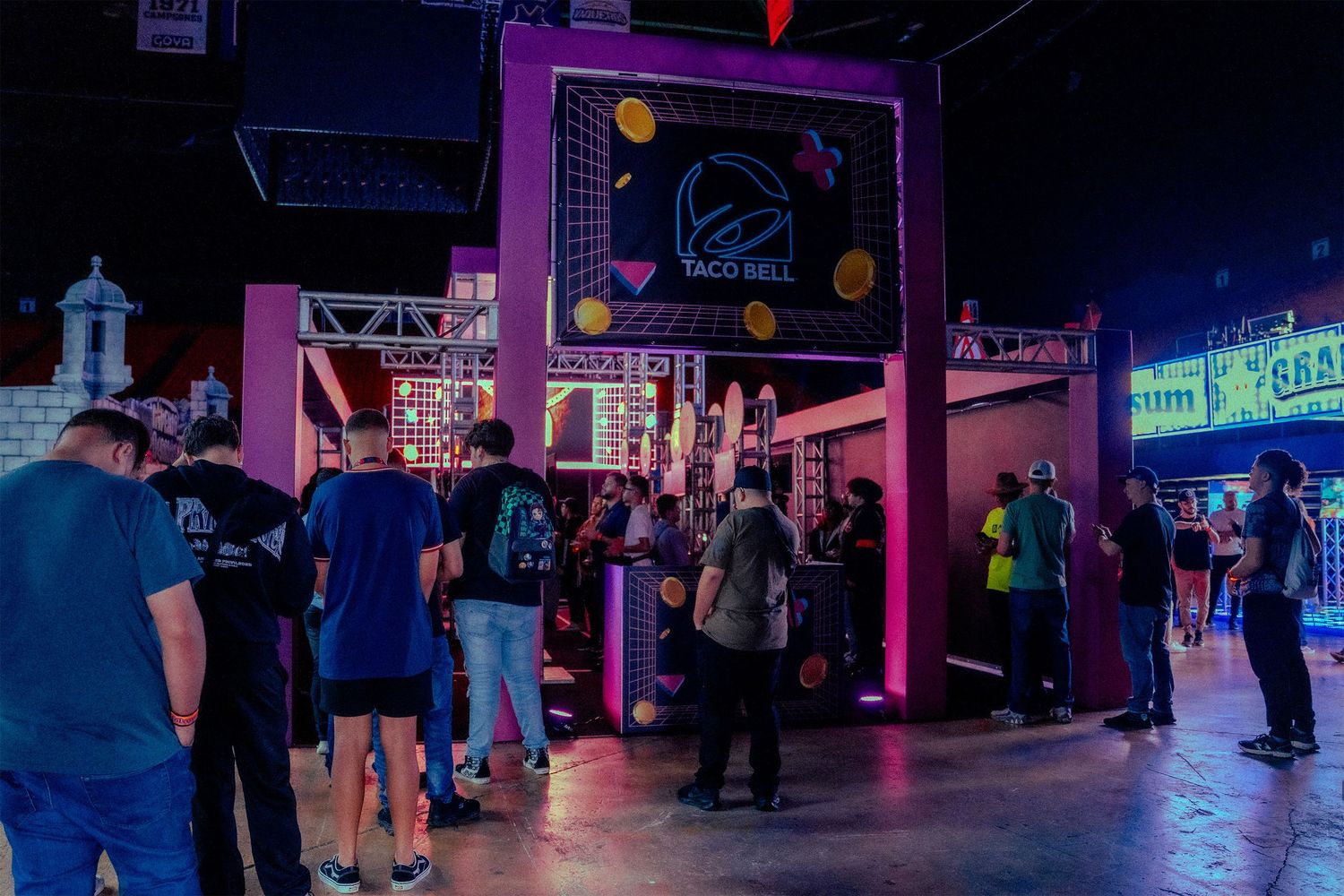 Dark arcade or gaming venue with purple neon lighting and crowd of spectators.
