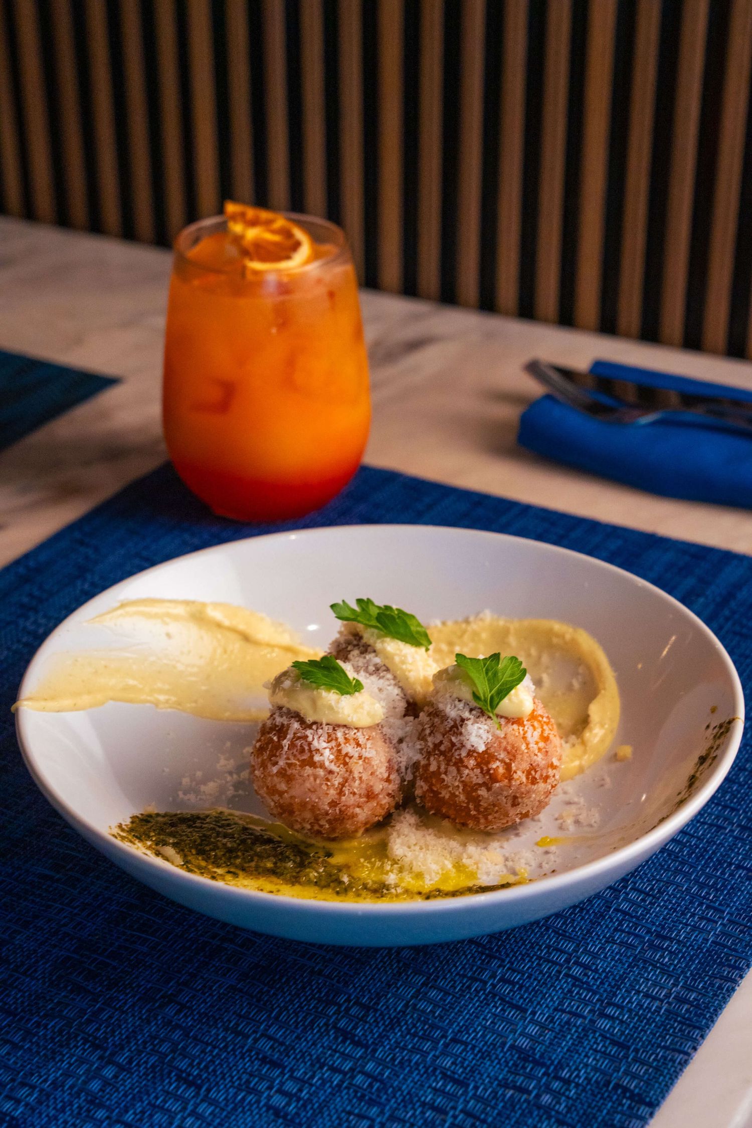 Meatballs in yellow sauce served on white plates with fresh herbs and blue table runner.