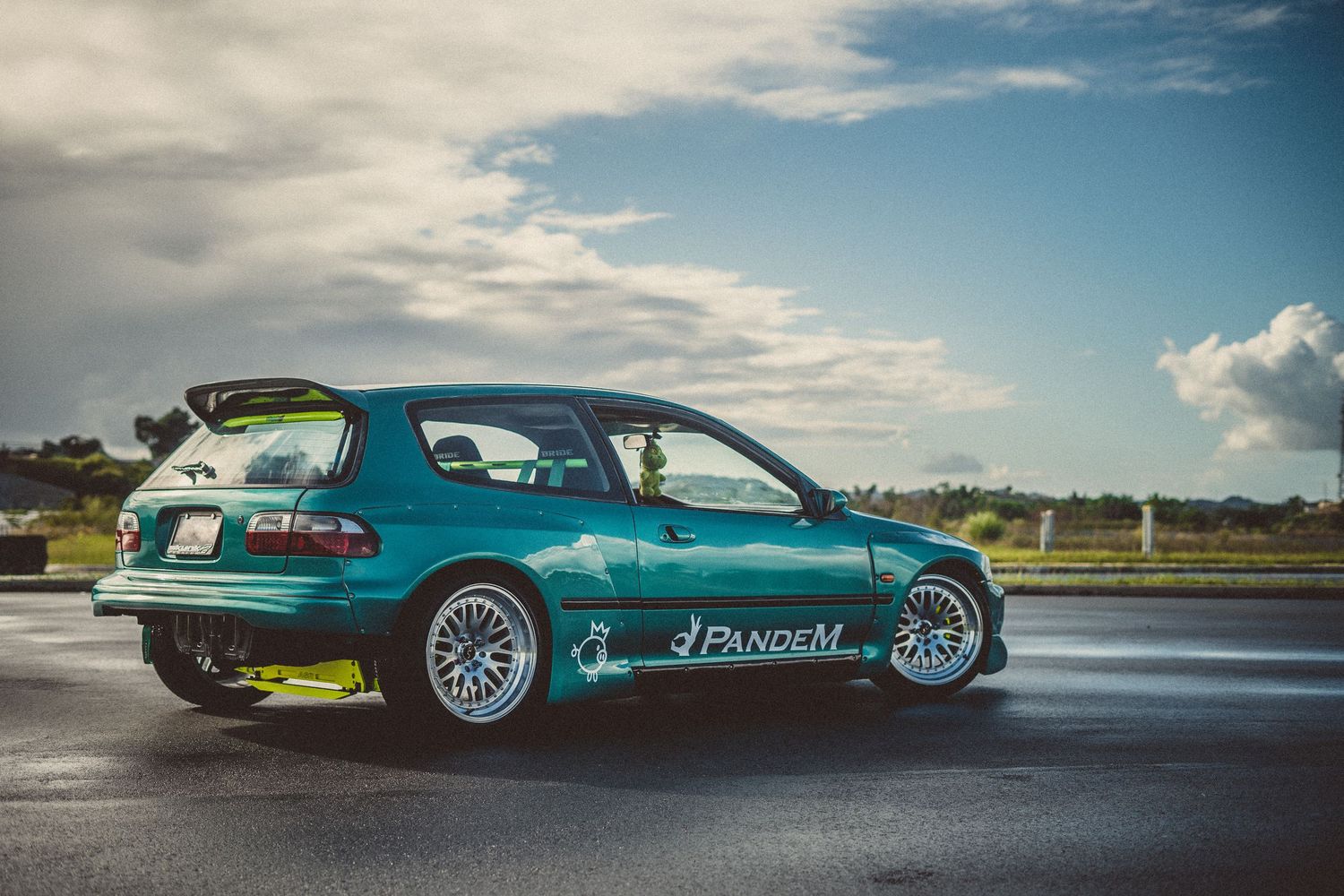 Turquoise sports car photographed from multiple angles against a cloudy sky backdrop.
