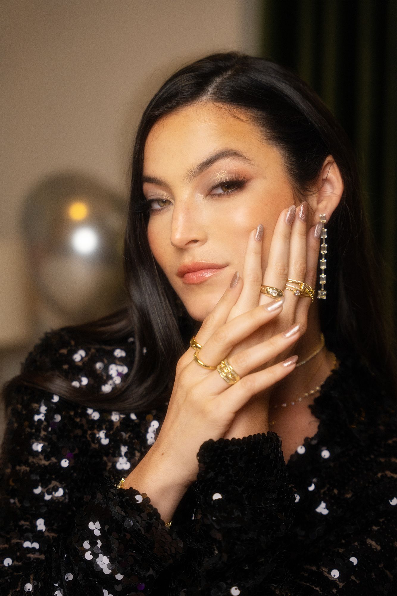 Glamour shot with sequined black dress and statement rings in evening lighting.