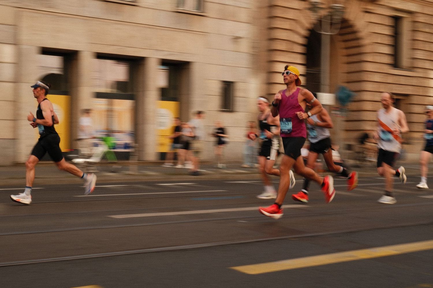 Runners in athletic gear sprinting past urban architecture during a marathon.