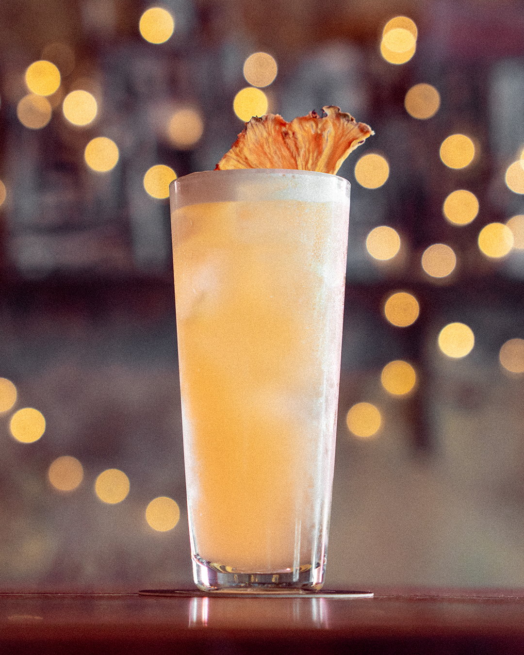 Frothy cocktail in rocks glass with bokeh lights in background.