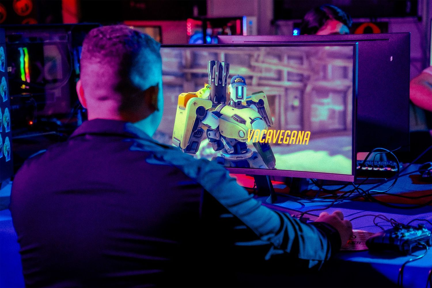 Gaming tournament setup with multiple monitors displaying gameplay under purple and red ambient lighting.