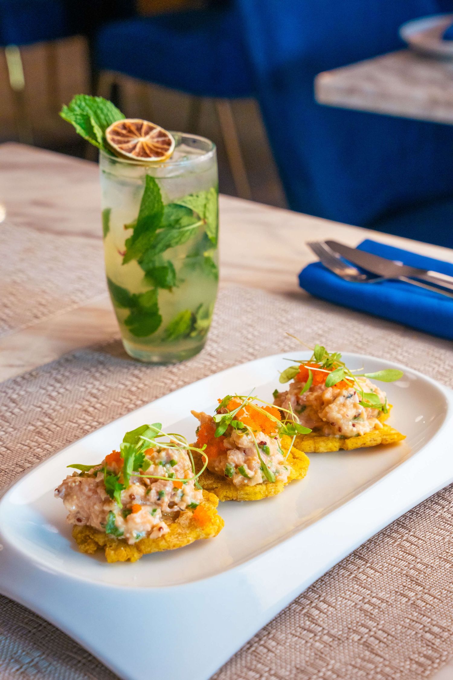 Tostadas topped with seafood salad and fresh herbs served on a white rectangular plate.