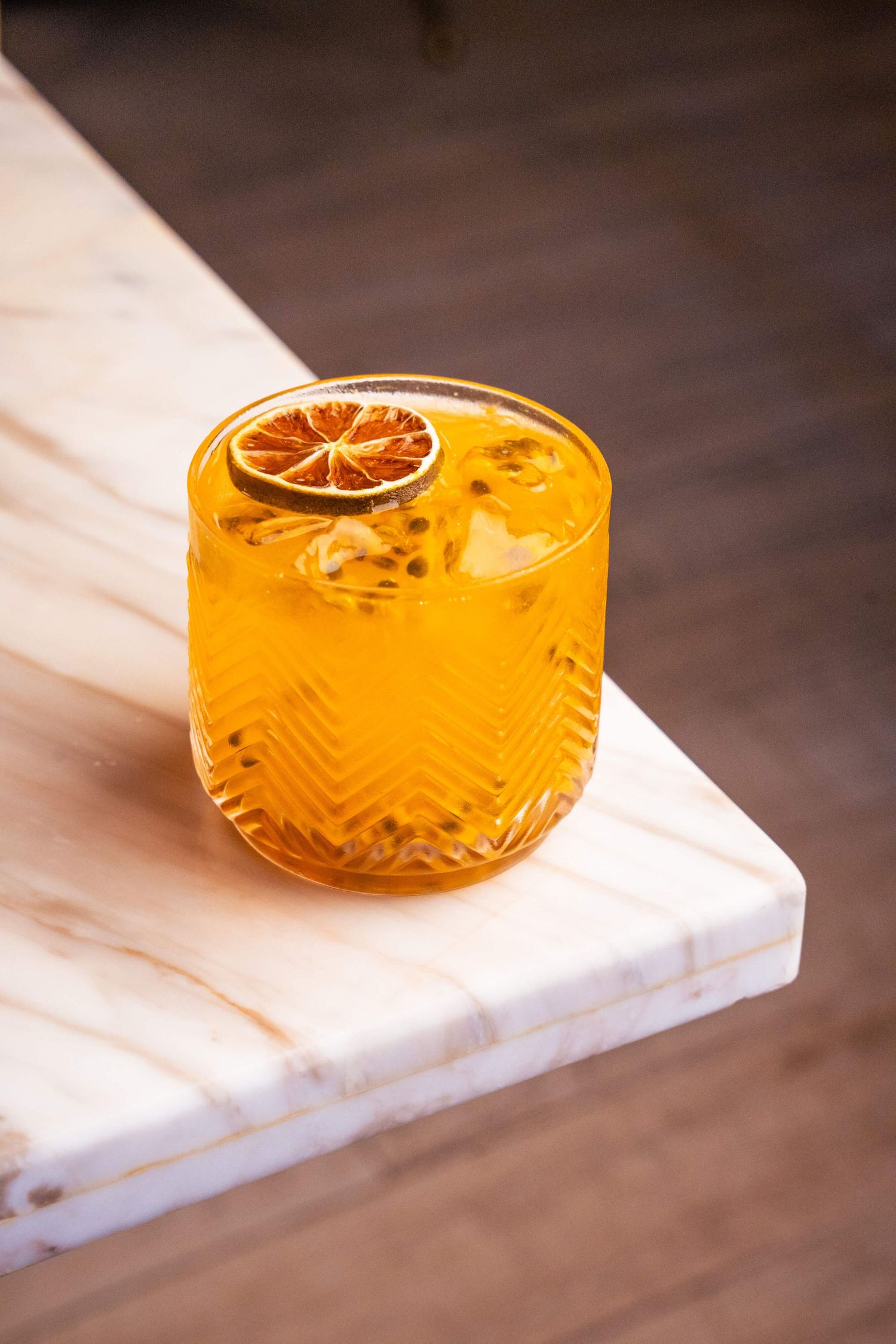 Orange cocktail garnished with a dried citrus wheel served in an etched coupe glass on white marble surface.