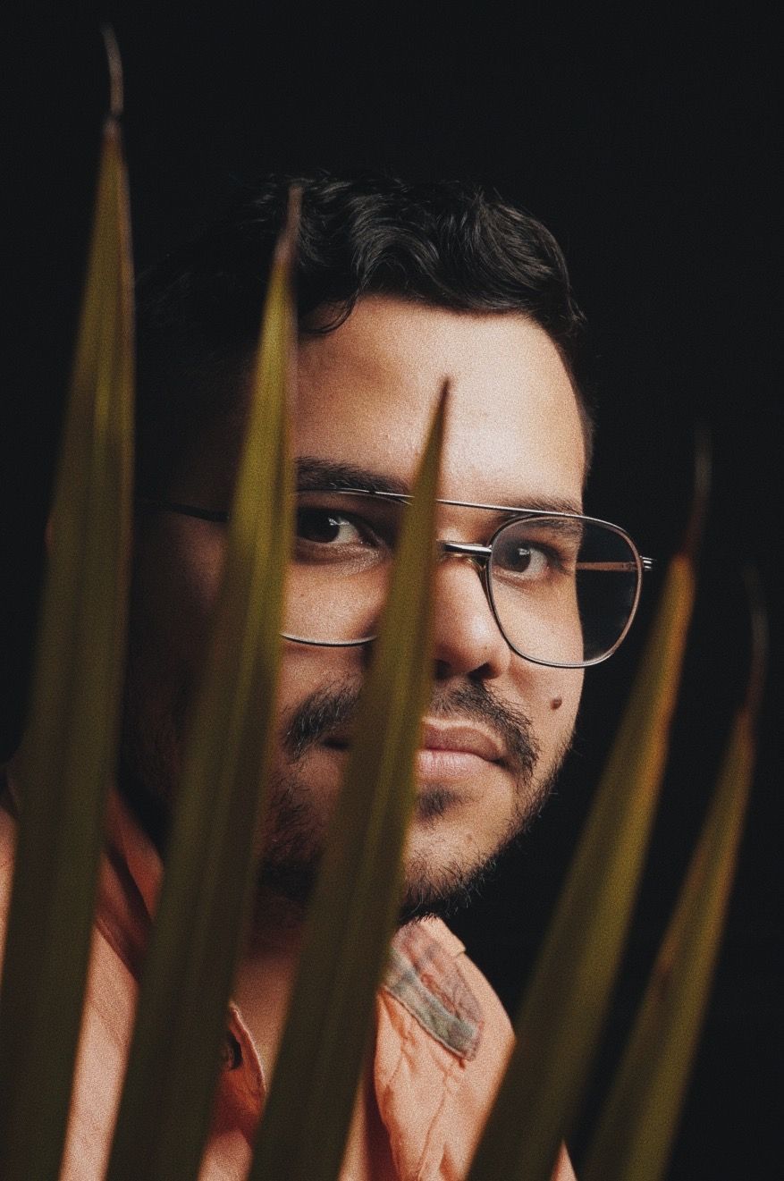 Artistic portrait through palm leaves with dramatic lighting and shadows.