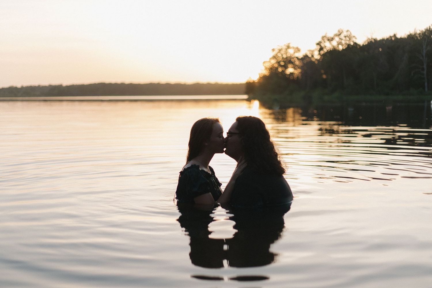 Two silhouettes share an intimate moment in calm waters during a serene sunset in Gun Barrel City, Texas