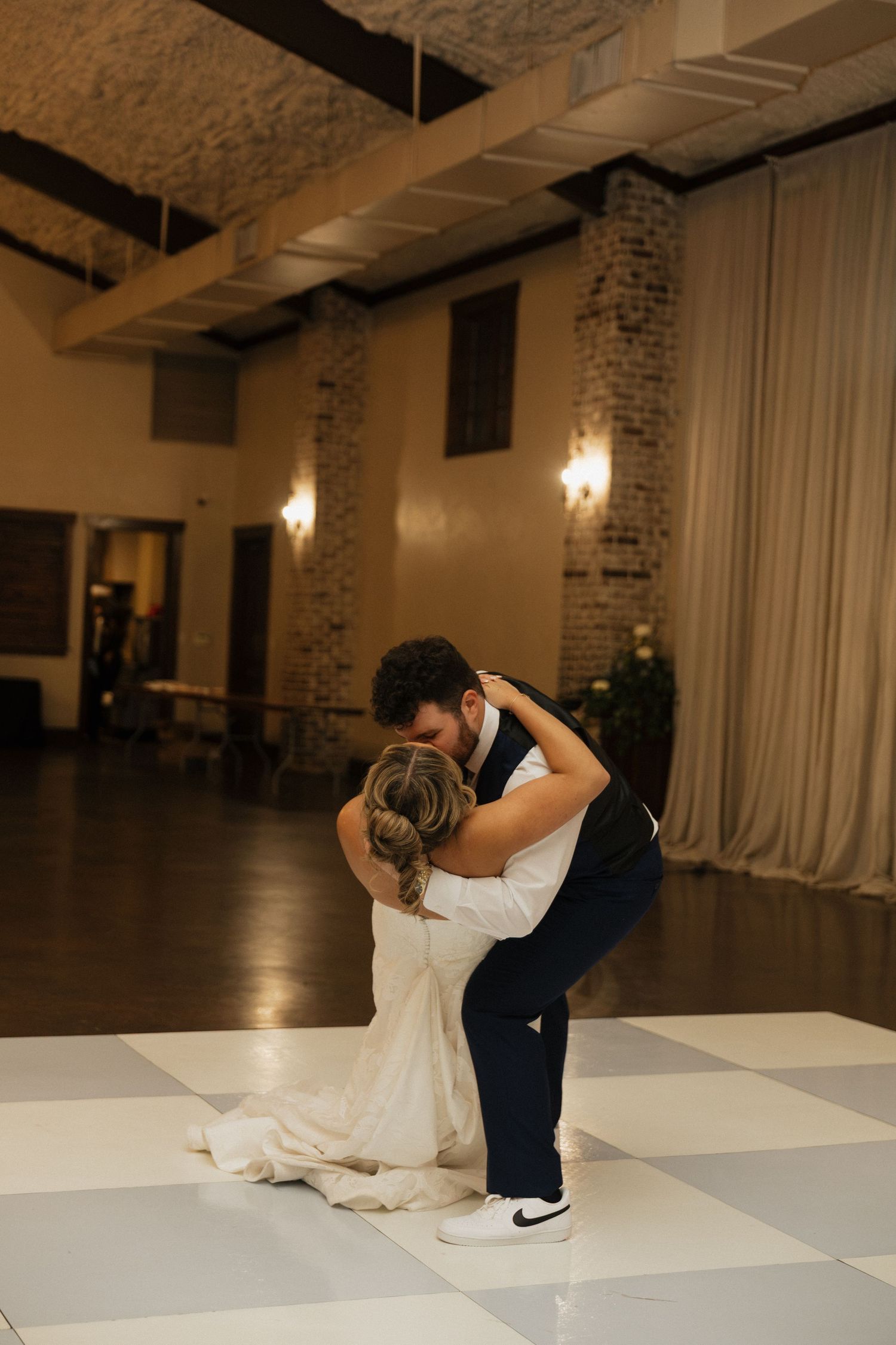 Bride and groom share a romantic dip on a black and white checkered dance floor at their wedding reception.