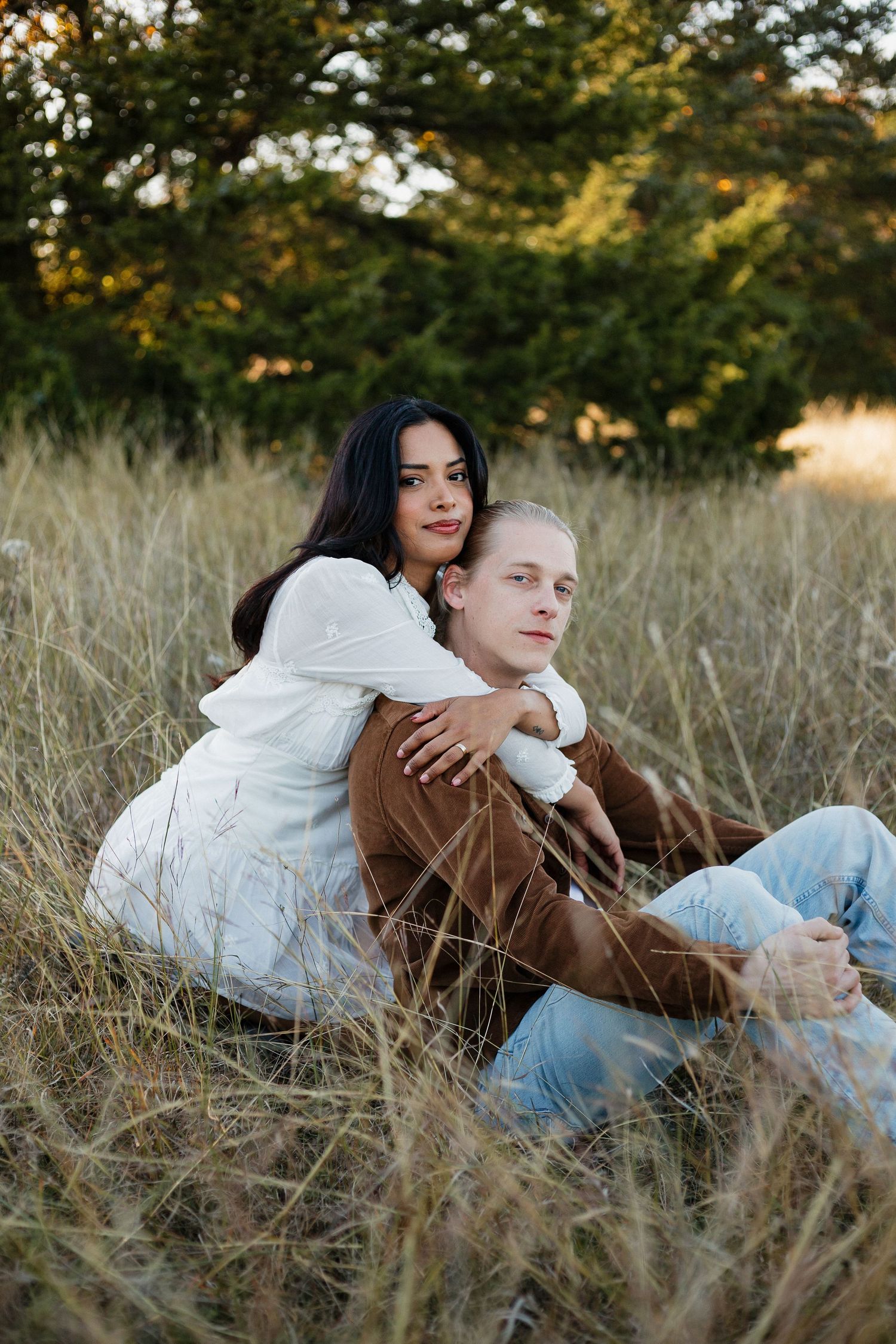 Couple sitting back-to-back in autumn field wearing coordinated casual outfits.