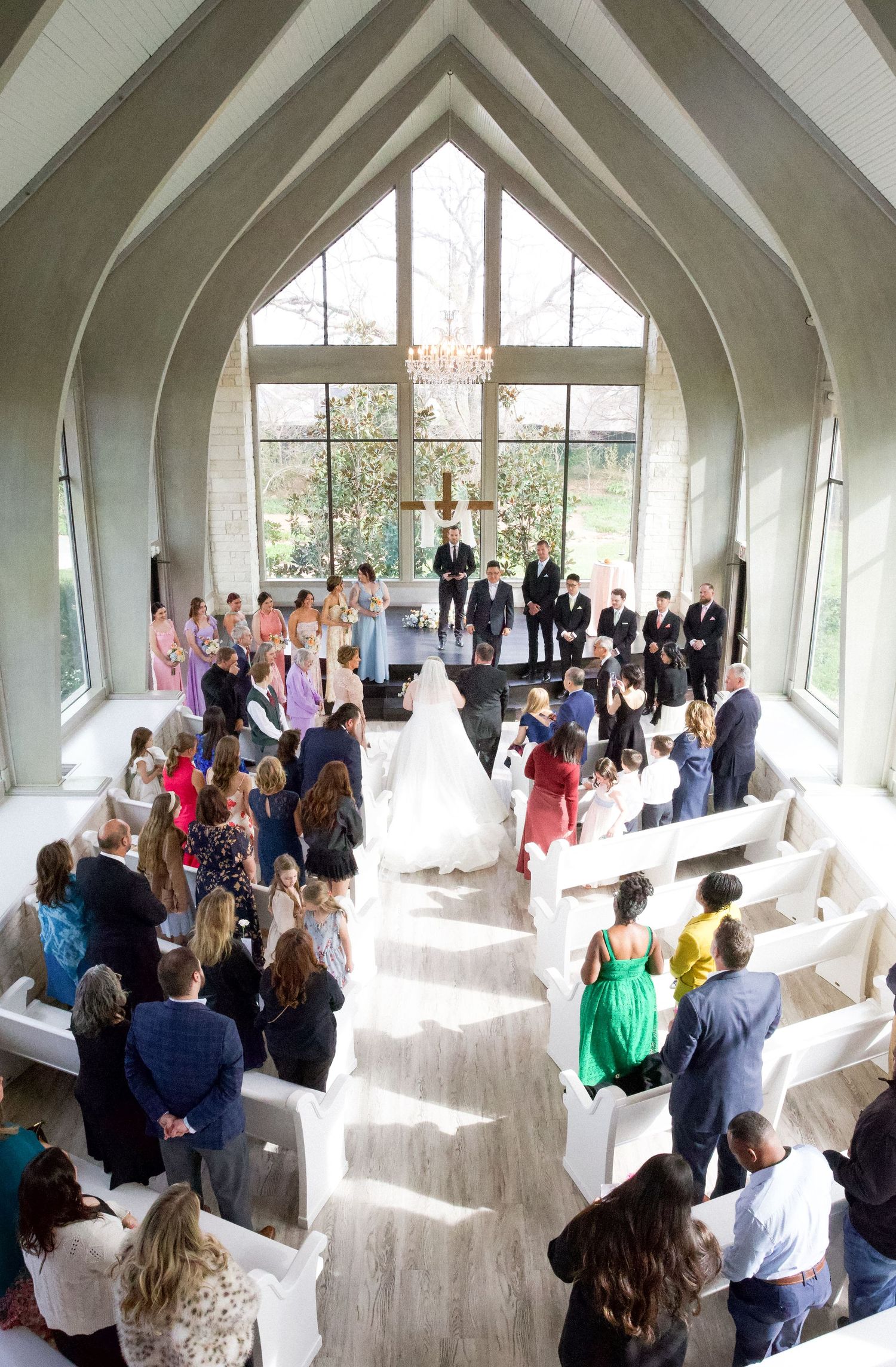Aerial view of elegant chapel wedding ceremony with bride walking down aisle toward altar.