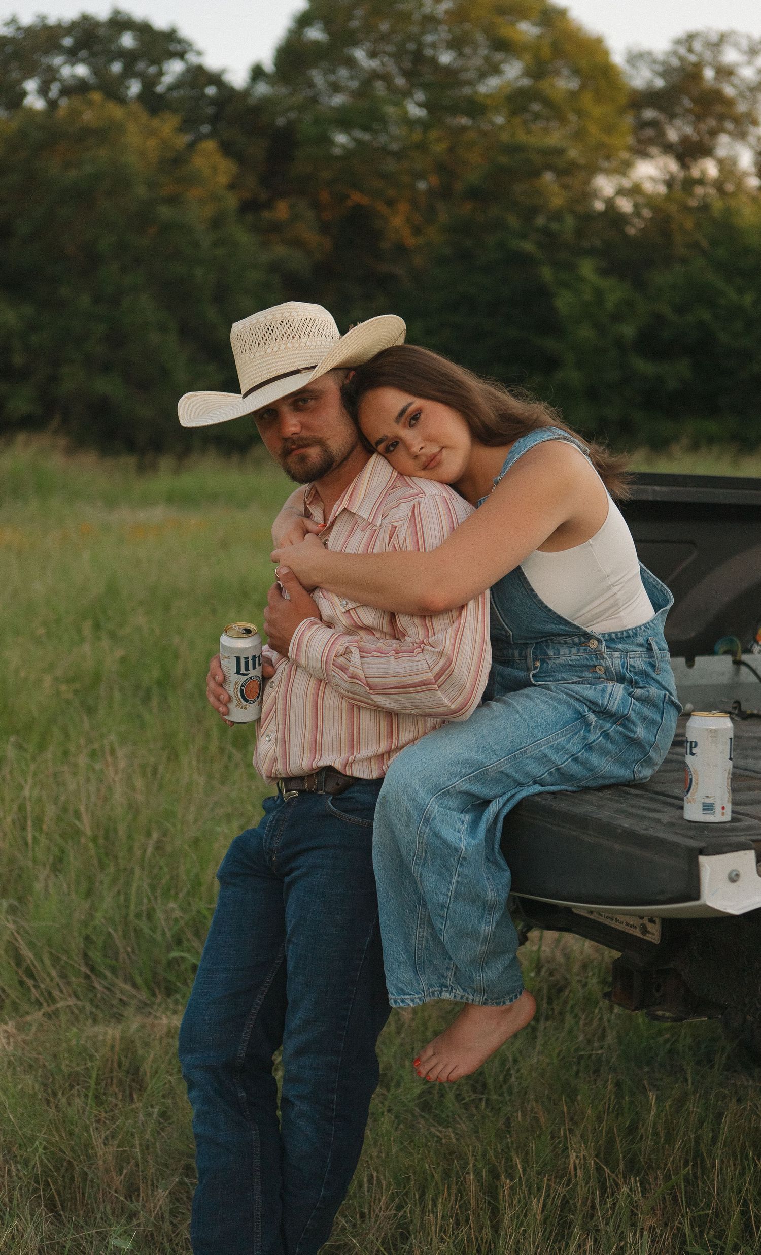 Couple sitting together on truck tailgate in rustic field setting.