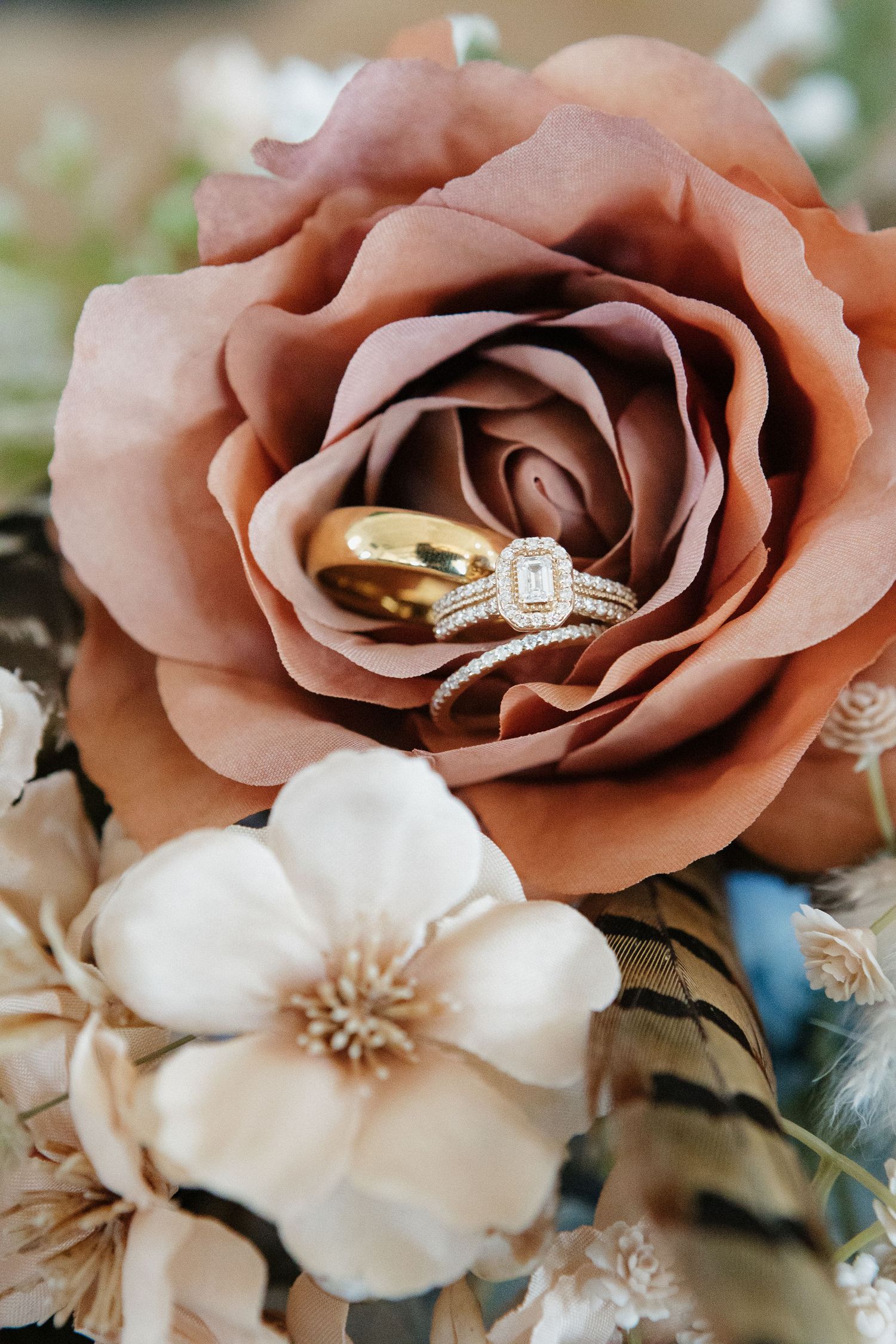 A series of dusty rose and white flowers with wedding rings nestled in their delicate petals.