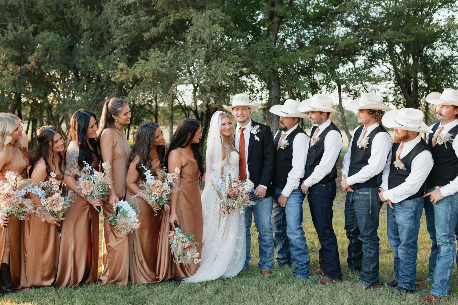 Large wedding party photo with bridesmaids in rust dresses and groomsmen in western attire.