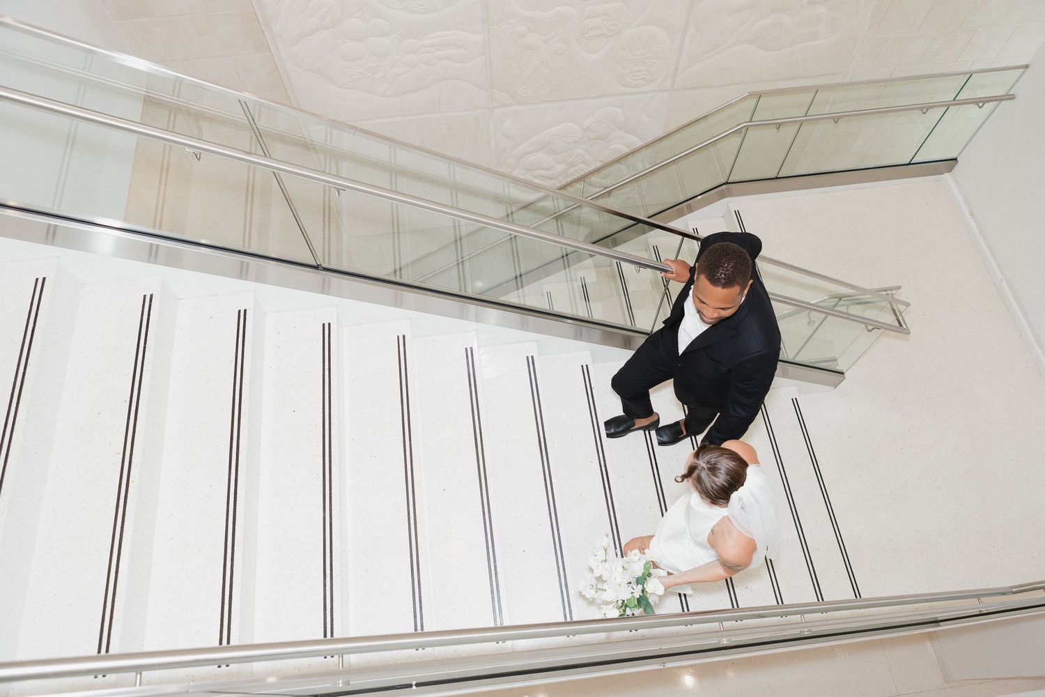 Skateboarder performs a trick on a slanted wall in a white minimalist indoor space.