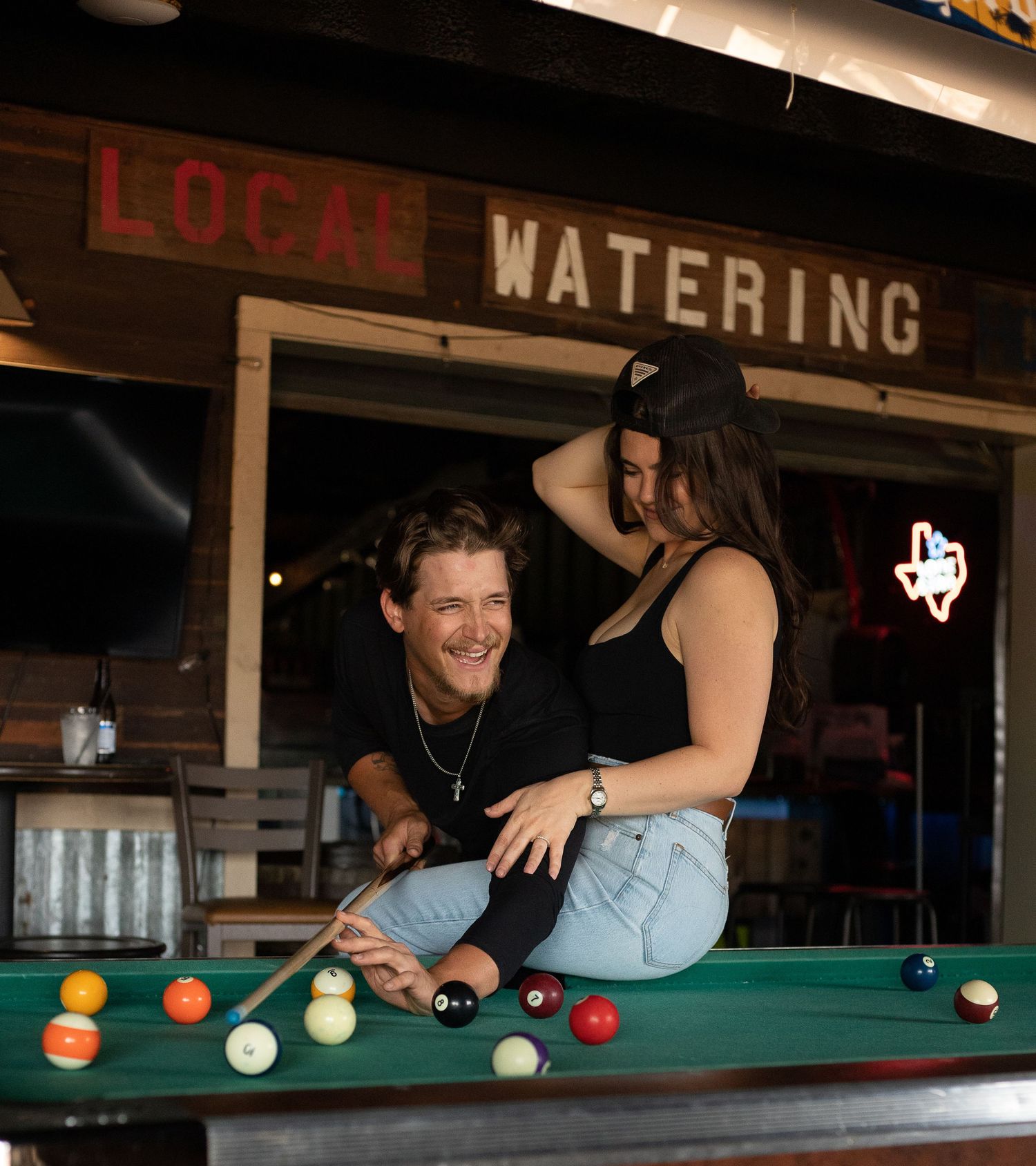 A couple enjoying a game of pool at Local Watering bar with colorful billiard balls scattered on the pool table in Caddo Mills, Texas
