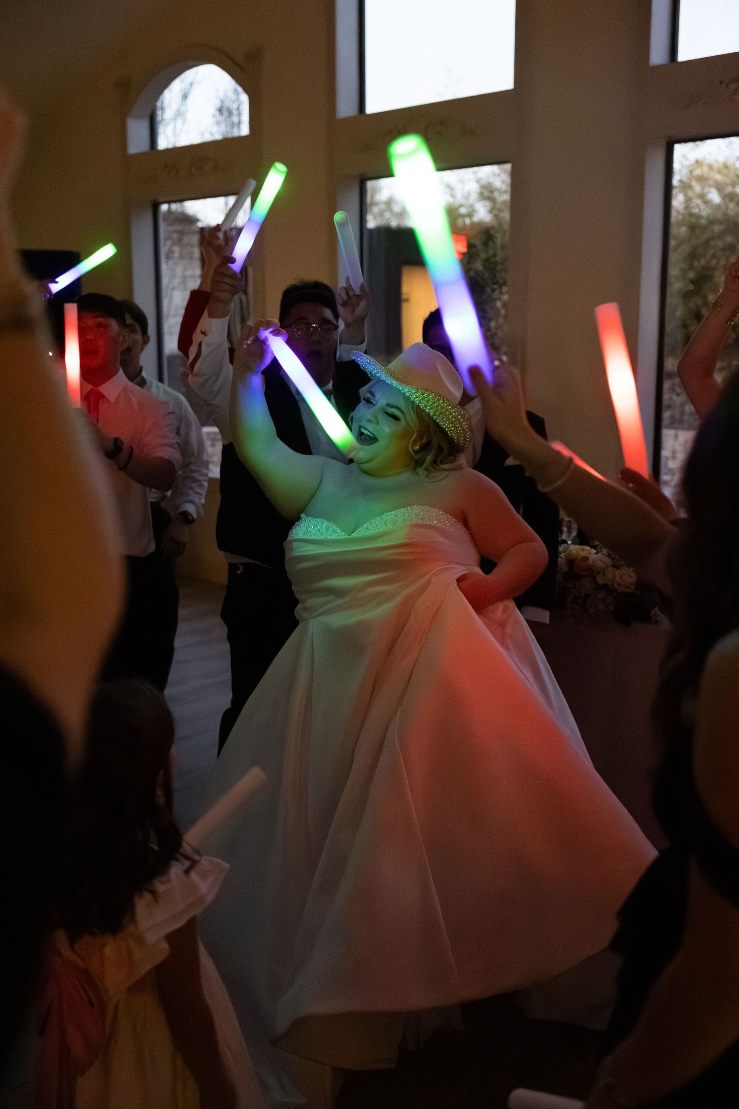 Bride dancing with glowing LED light sabers at lively wedding reception party.