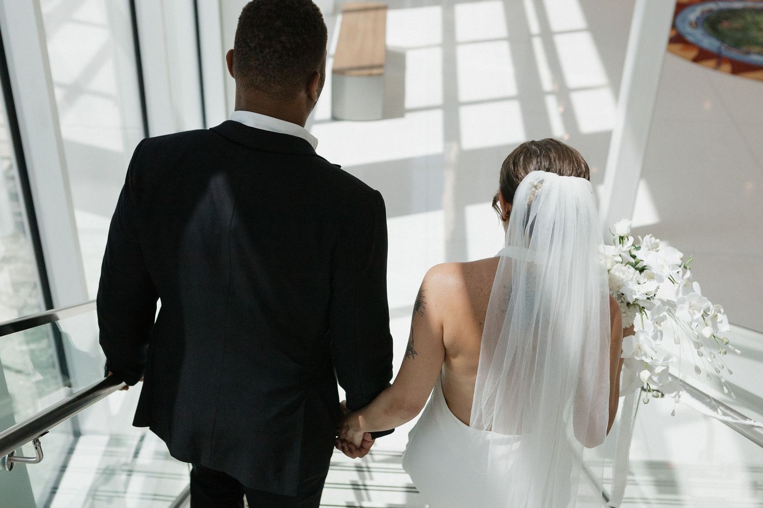 A bride and groom stand together in a bright modern building with large windows and white decor.