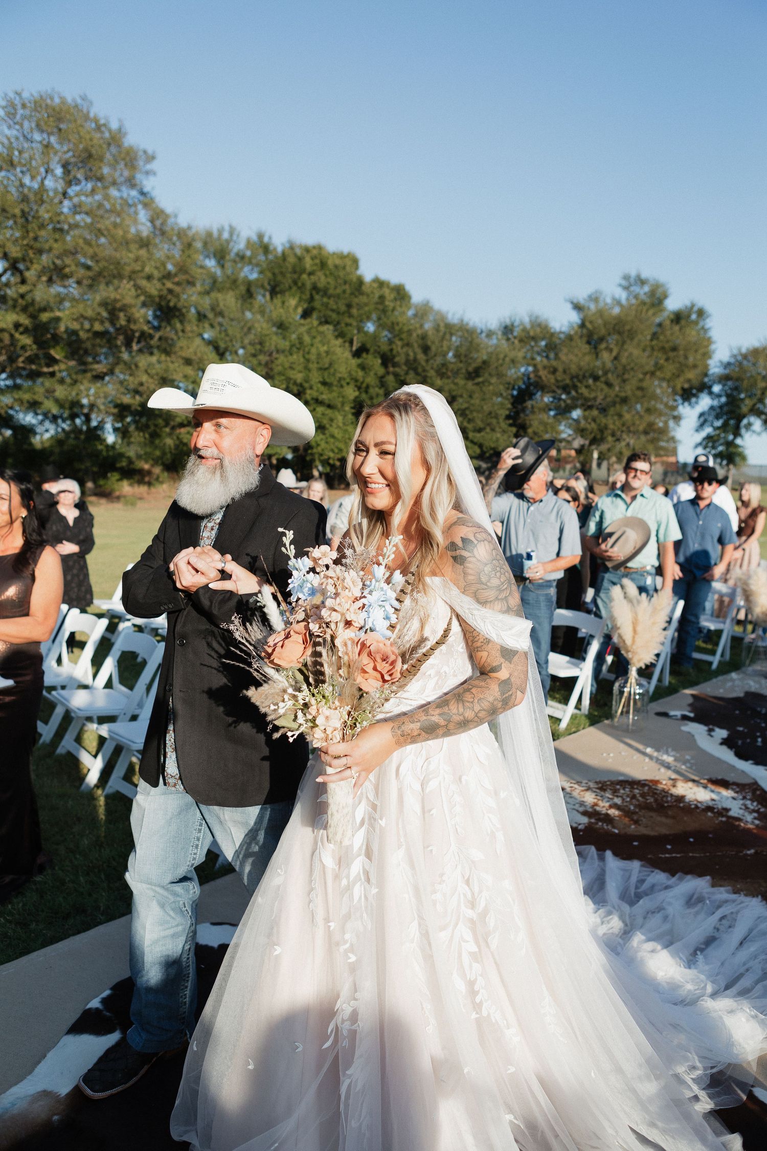 Outdoor wedding ceremony with guests seated in white chairs under blue sky.