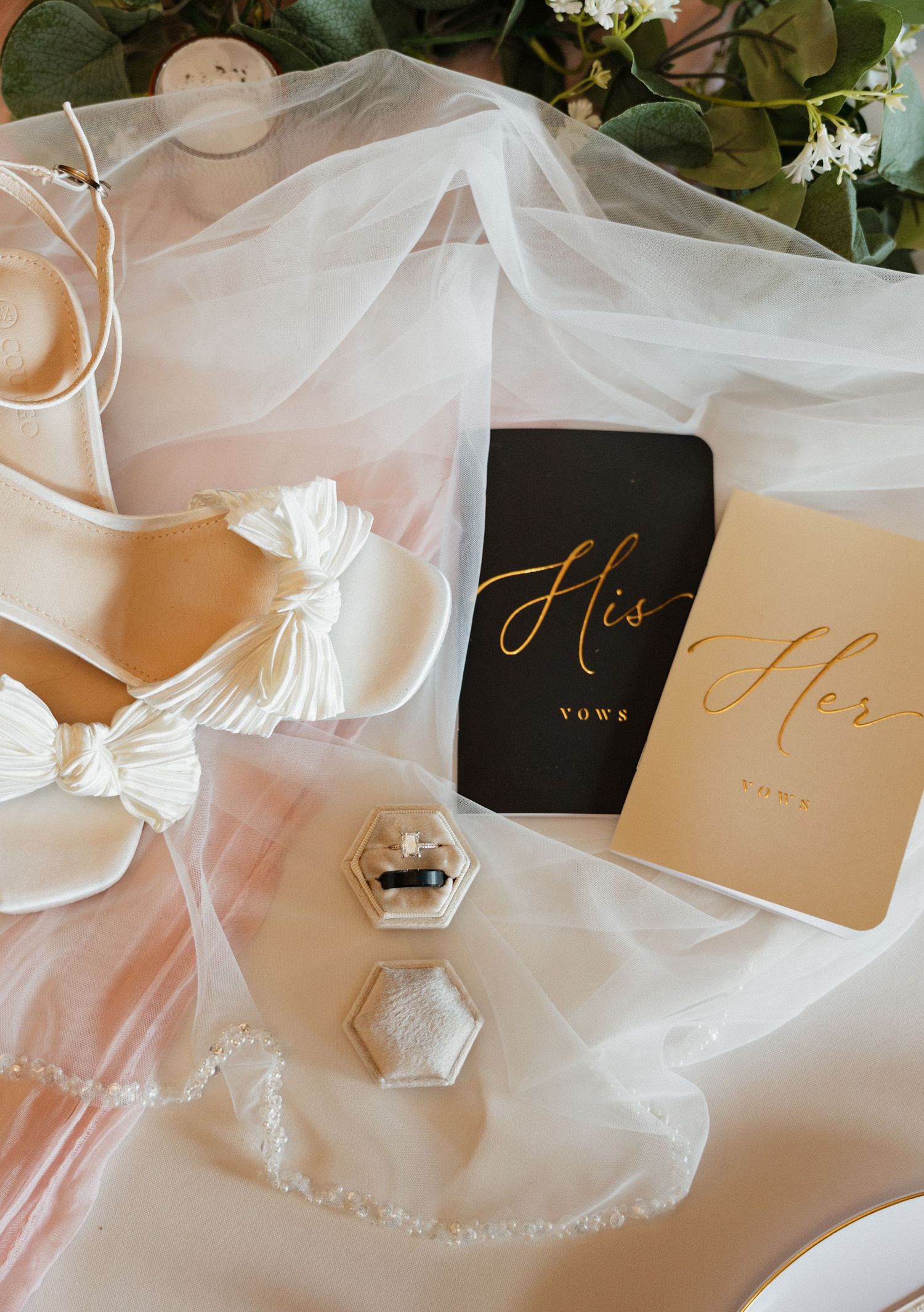 Elegant wedding flat lay with bridal heels, veil, his and her vow books, and a diamond ring box.