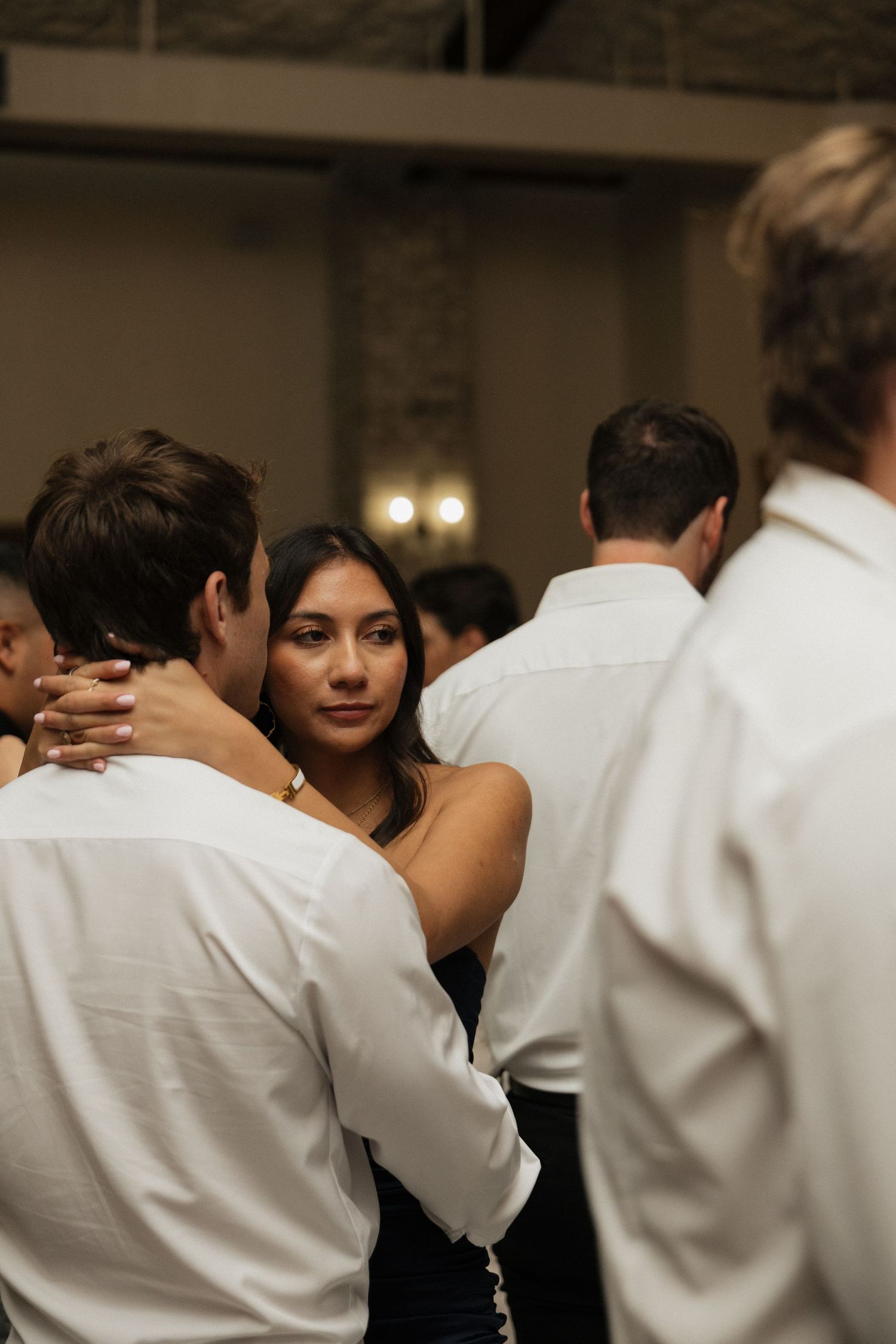 Wedding guest in black dress dances closely with partner amid crowded reception dance floor.