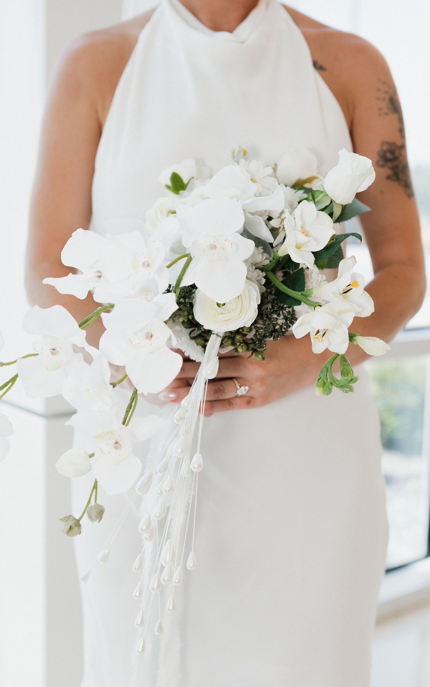 A white orchid and rose bridal bouquet with cascading ribbons held against an elegant white wedding dress.