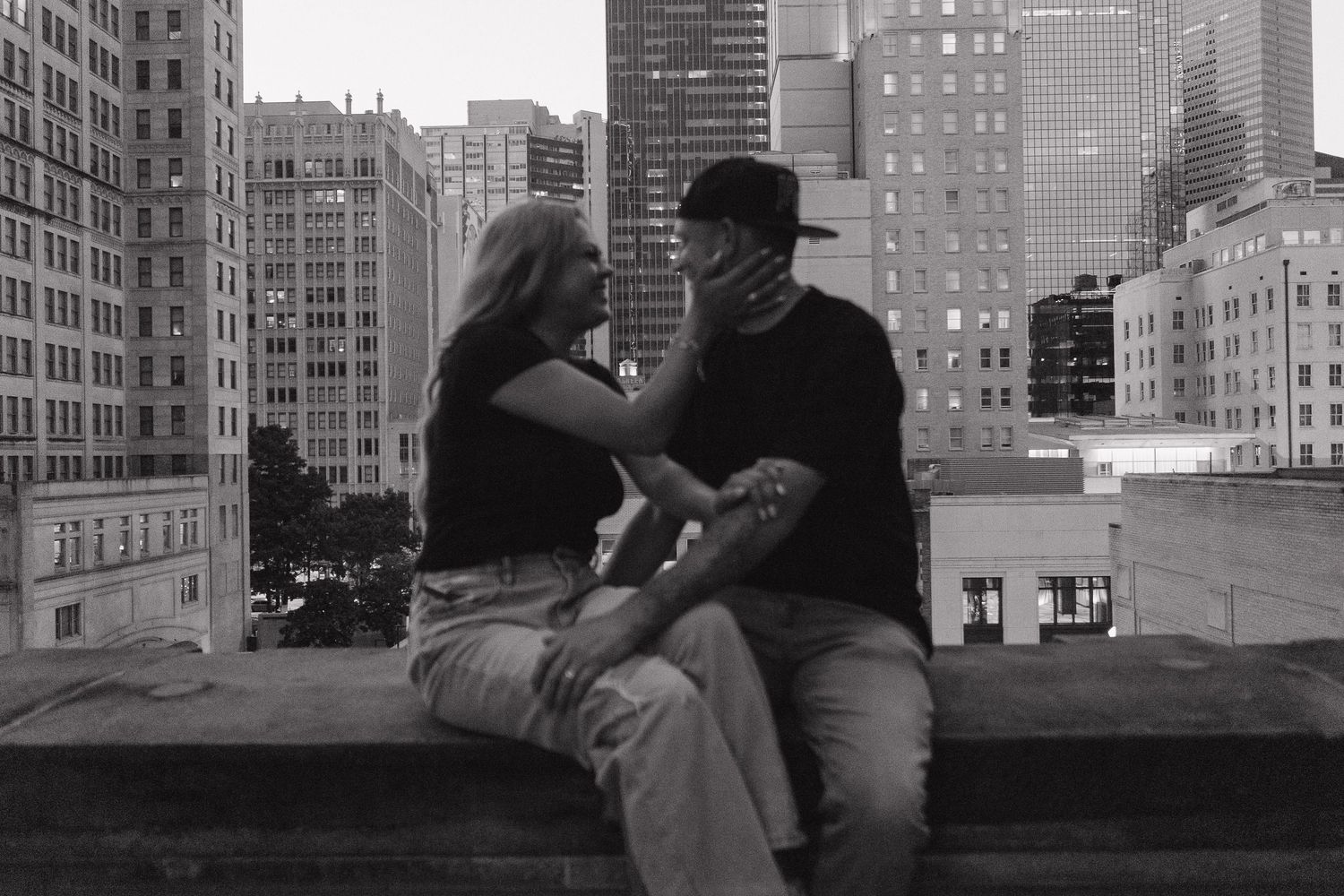 A black and white photo montage shows people sitting along a wall in an urban setting with tall buildings in the background. Downtown Dallas