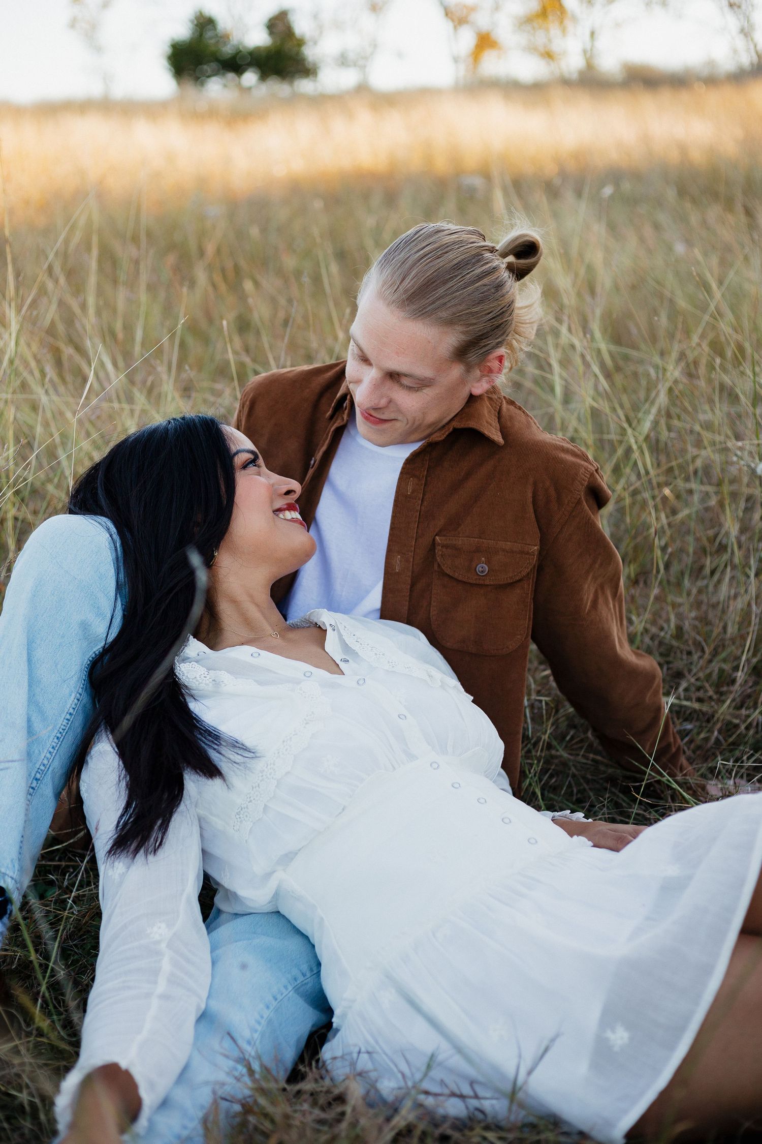 Romantic couple relaxing in tall grass during golden hour photoshoot.